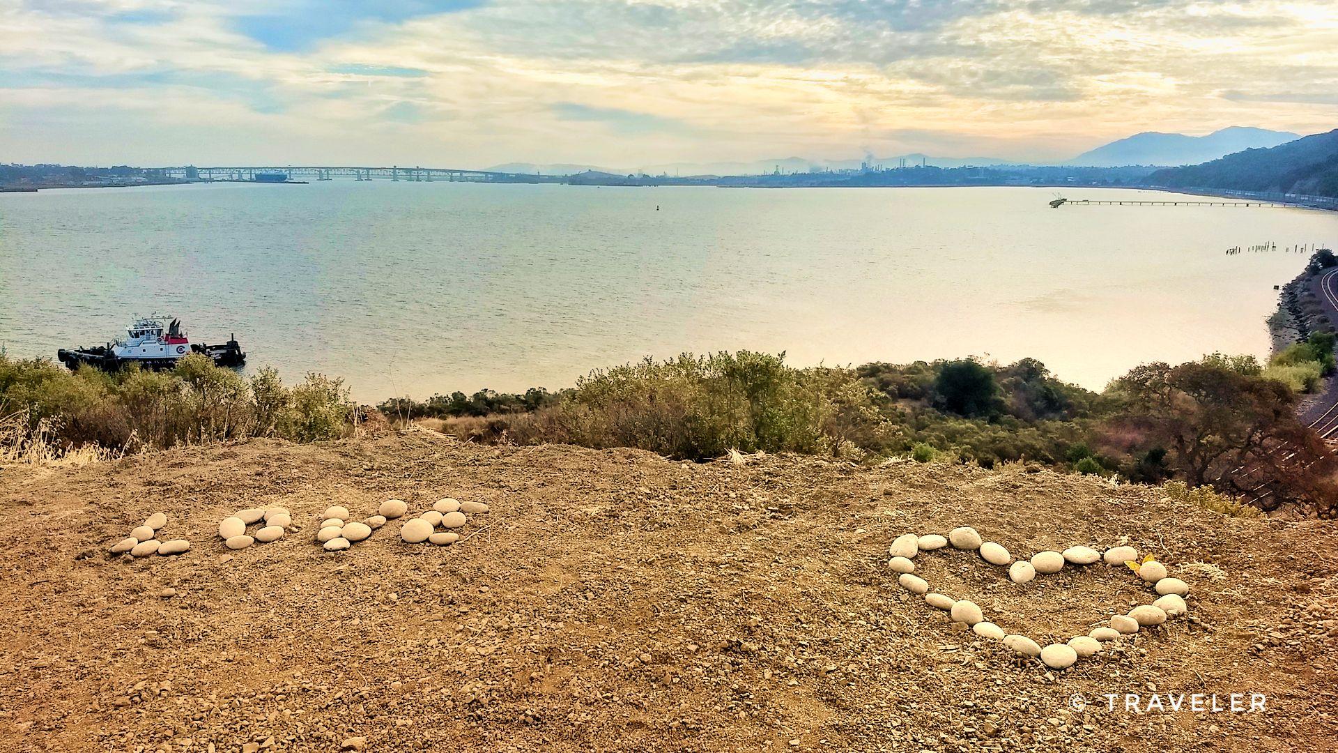 Rocks spell 'LOVE' and form a heart overlooking a wide bay with a distant bridge.