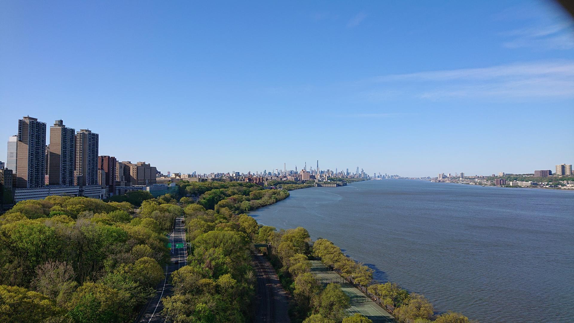 Wide river with city skyline, green trees, and clear blue sky.
