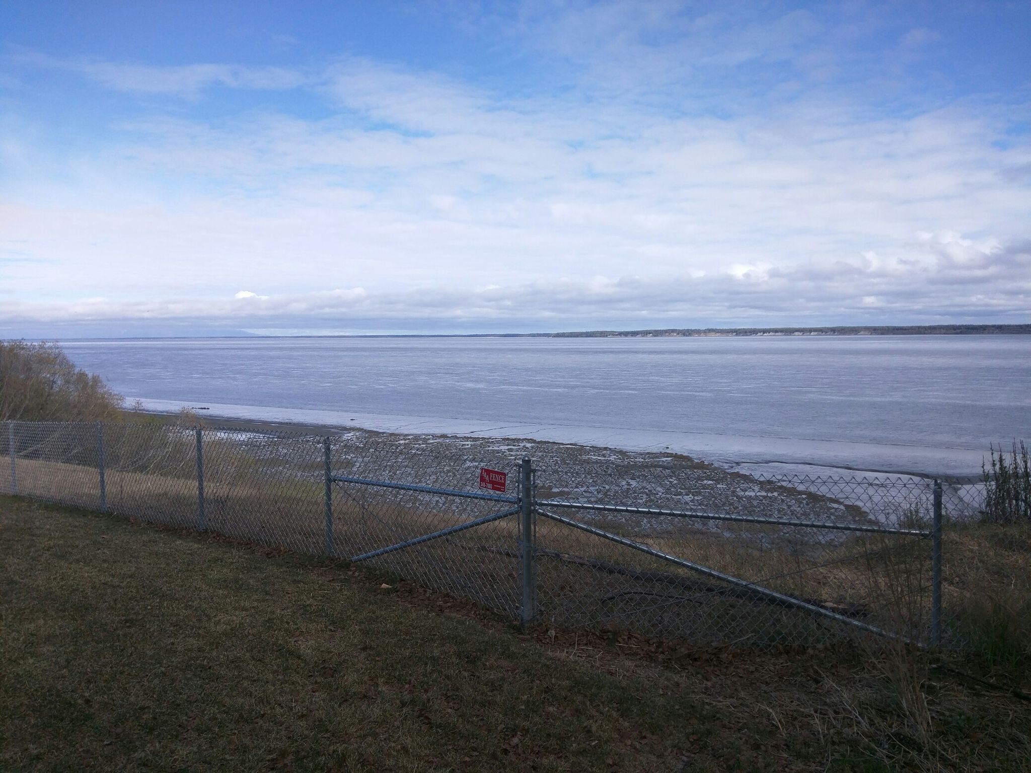 Chain link fence overlooking a calm body of water under an overcast sky. - Tony Knowles Coastal Trail
