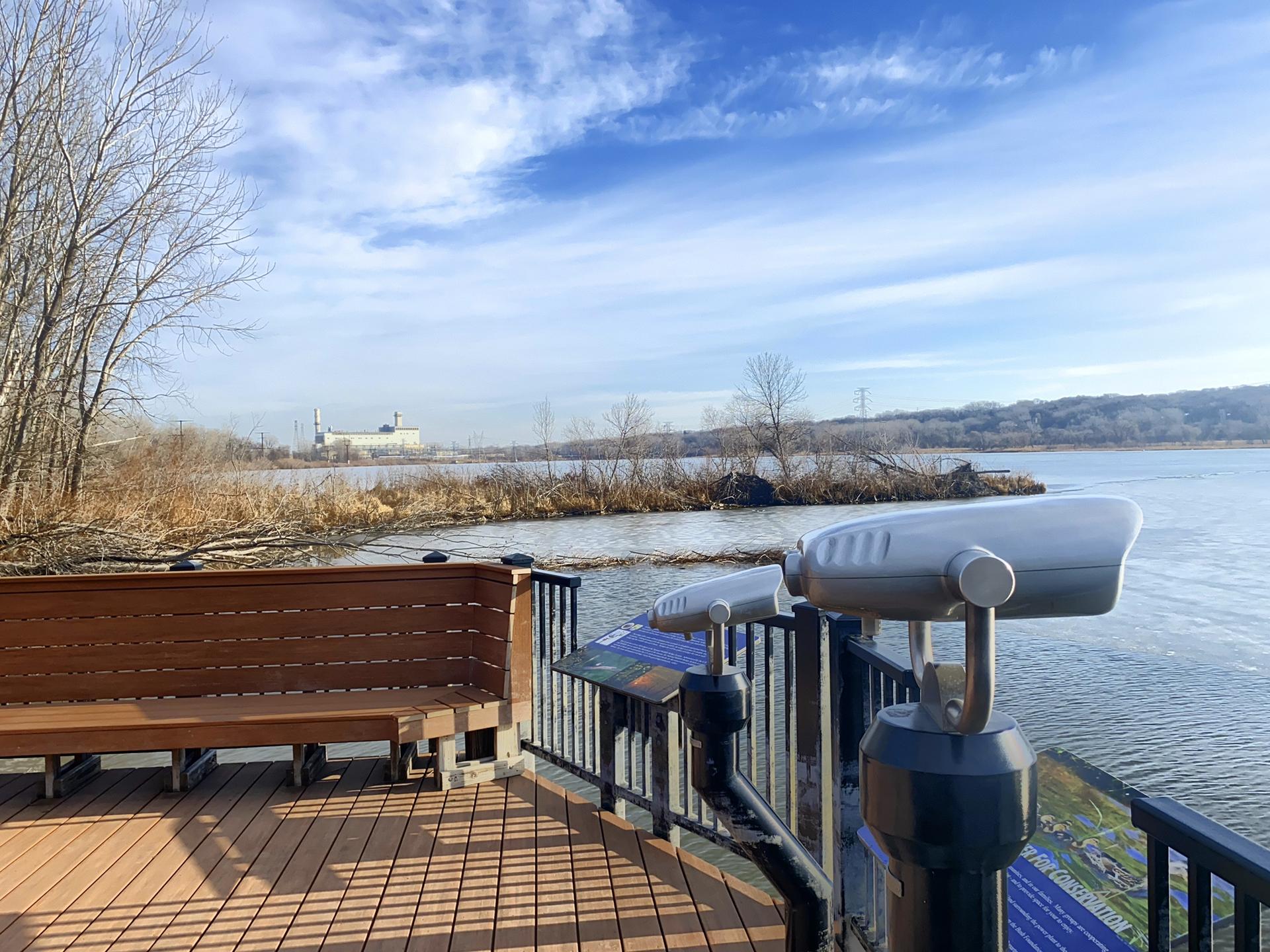 Observation deck with binoculars overlooking a river under a blue sky.