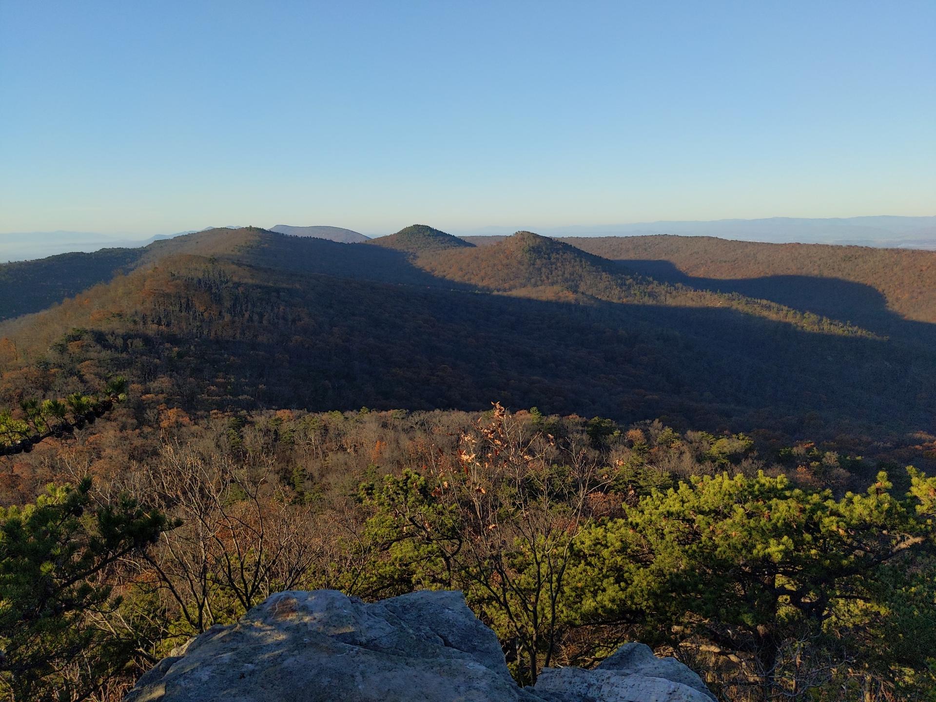 Sunny view of forested mountain ridges with long shadows under a clear blue sky.