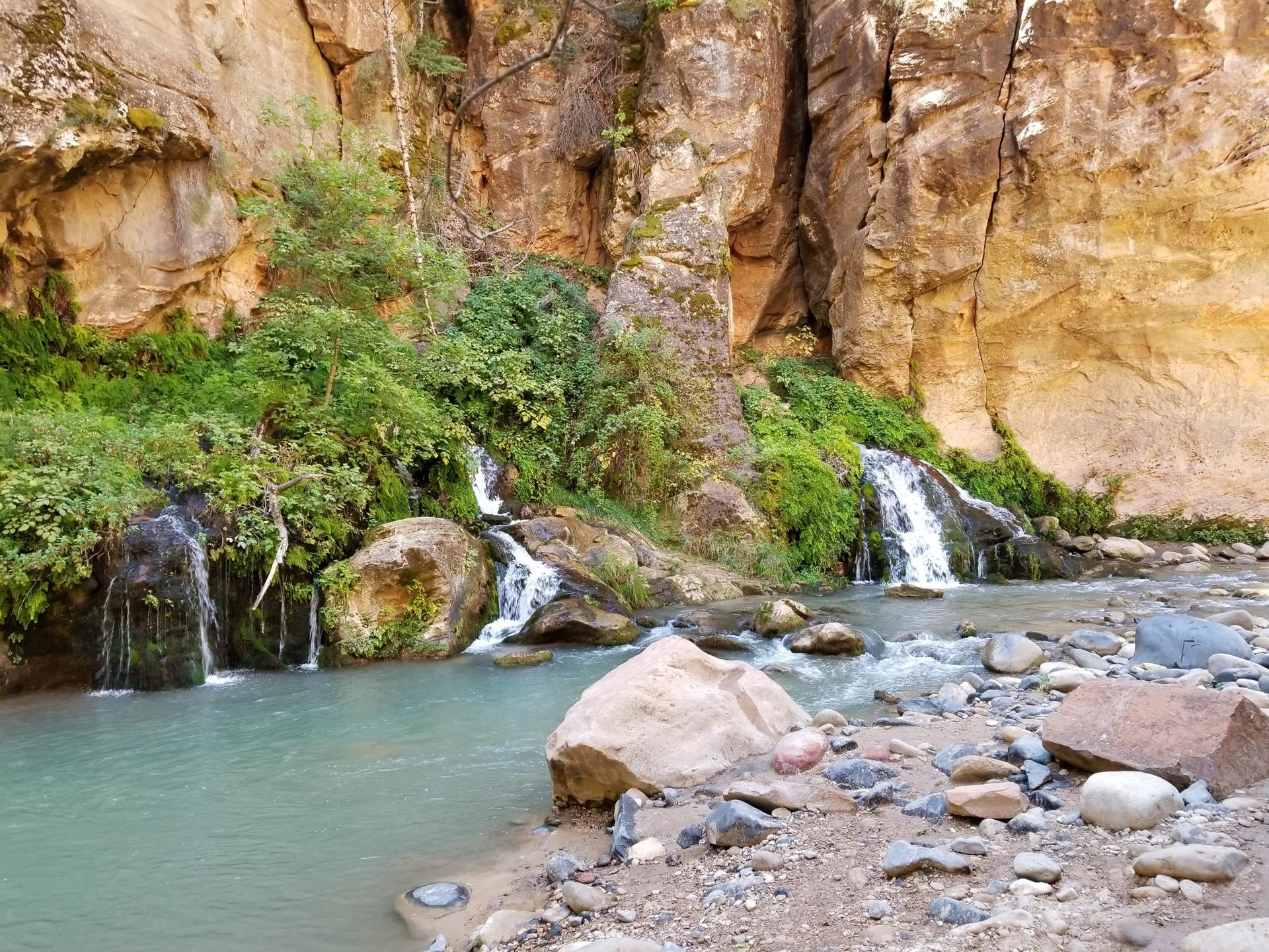Clear river flows past rocky banks with several small waterfalls.