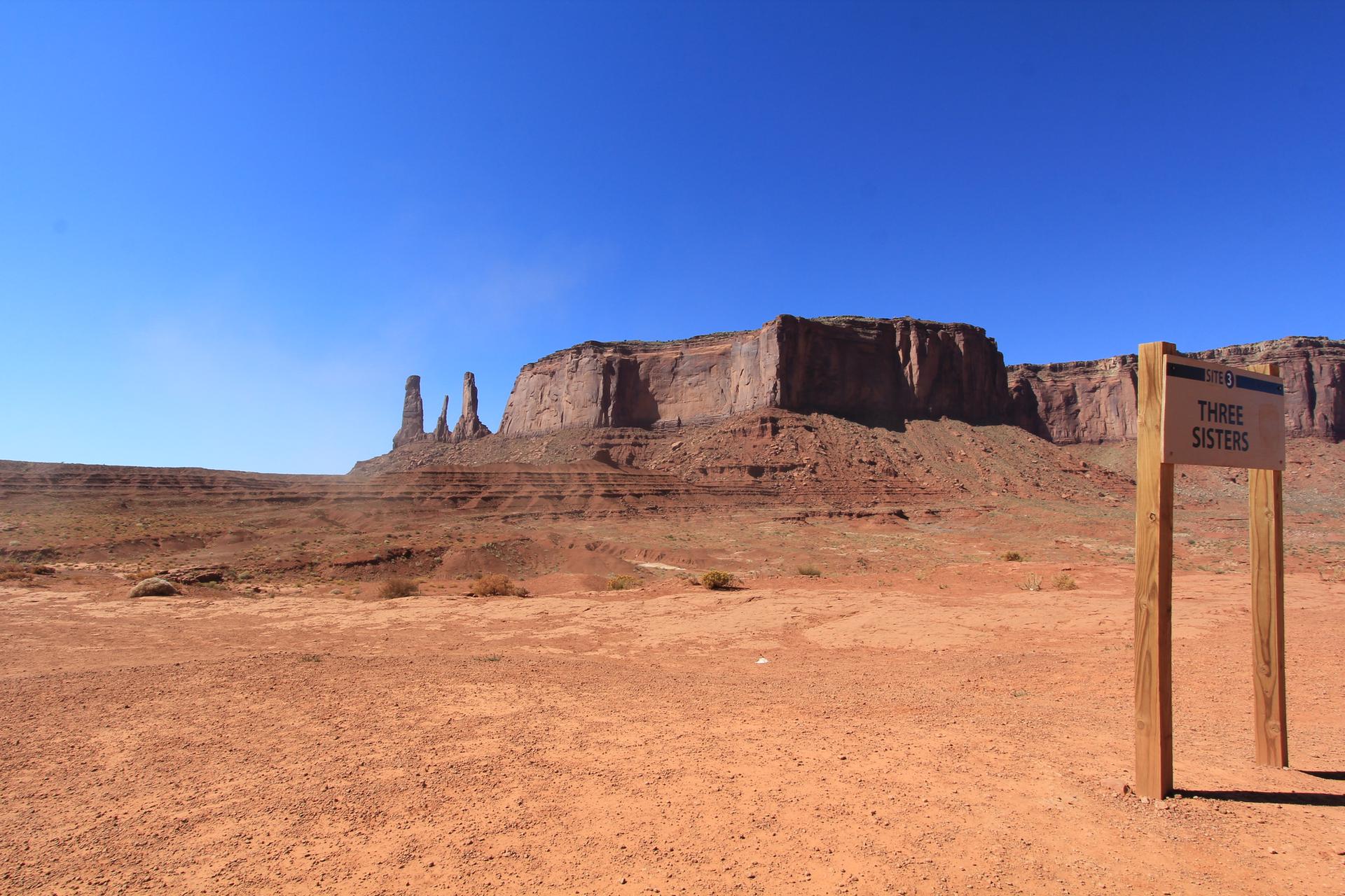 Expansive desert with distant red rock formations and a wooden sign on the right.