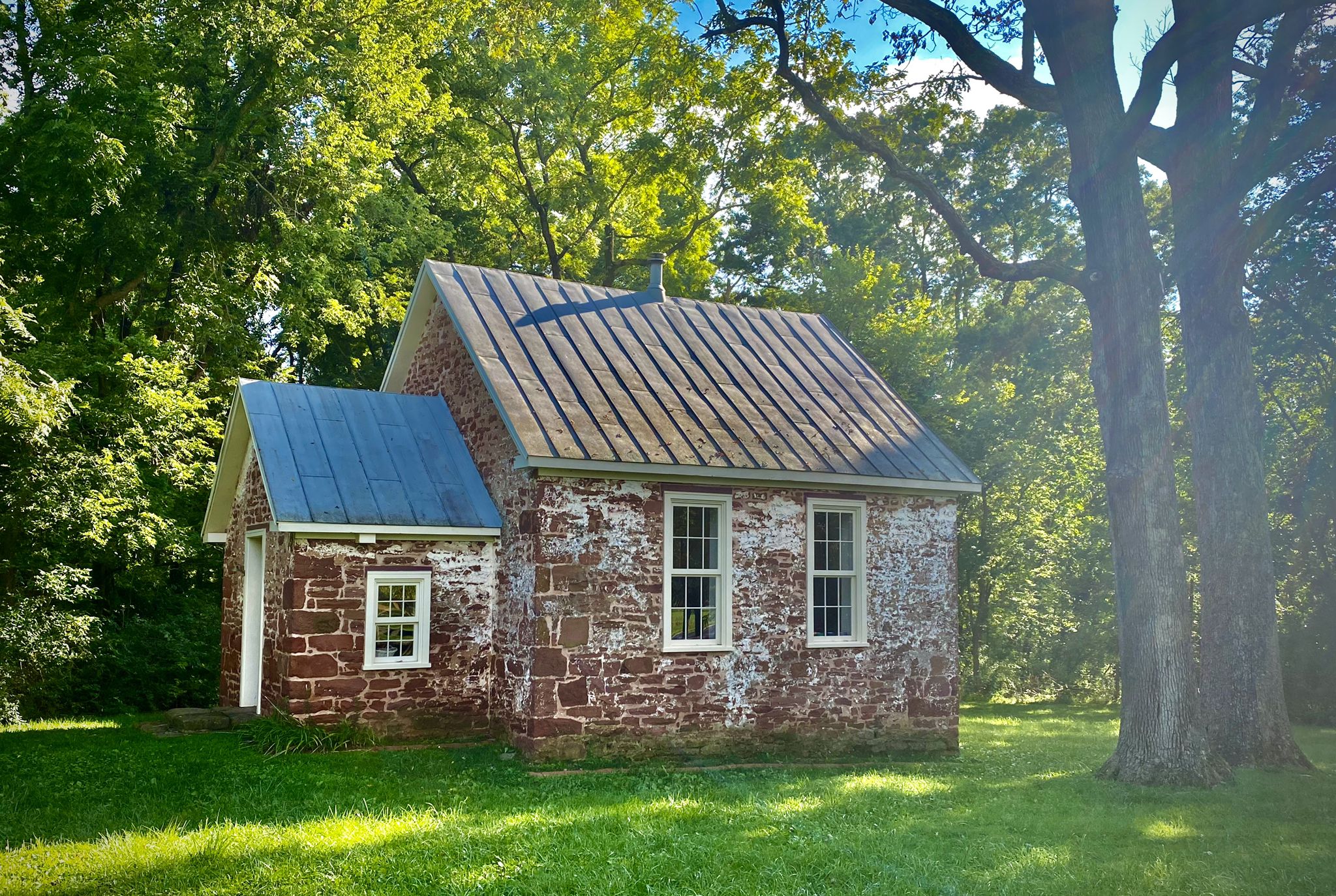 Small stone building with a metal roof surrounded by green trees in sunlight. - Montevideo Road – Seneca Schoolhouse loop from Seneca