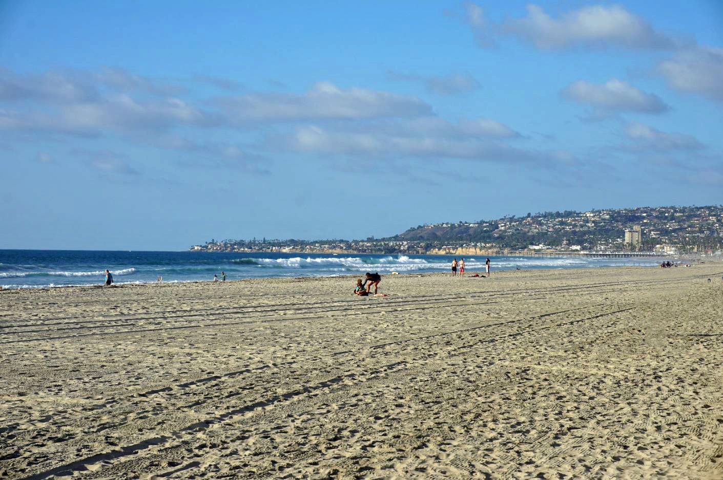 Sunny beach with ocean waves, distant city, and people enjoying the sand. - Ocean Front Walk
