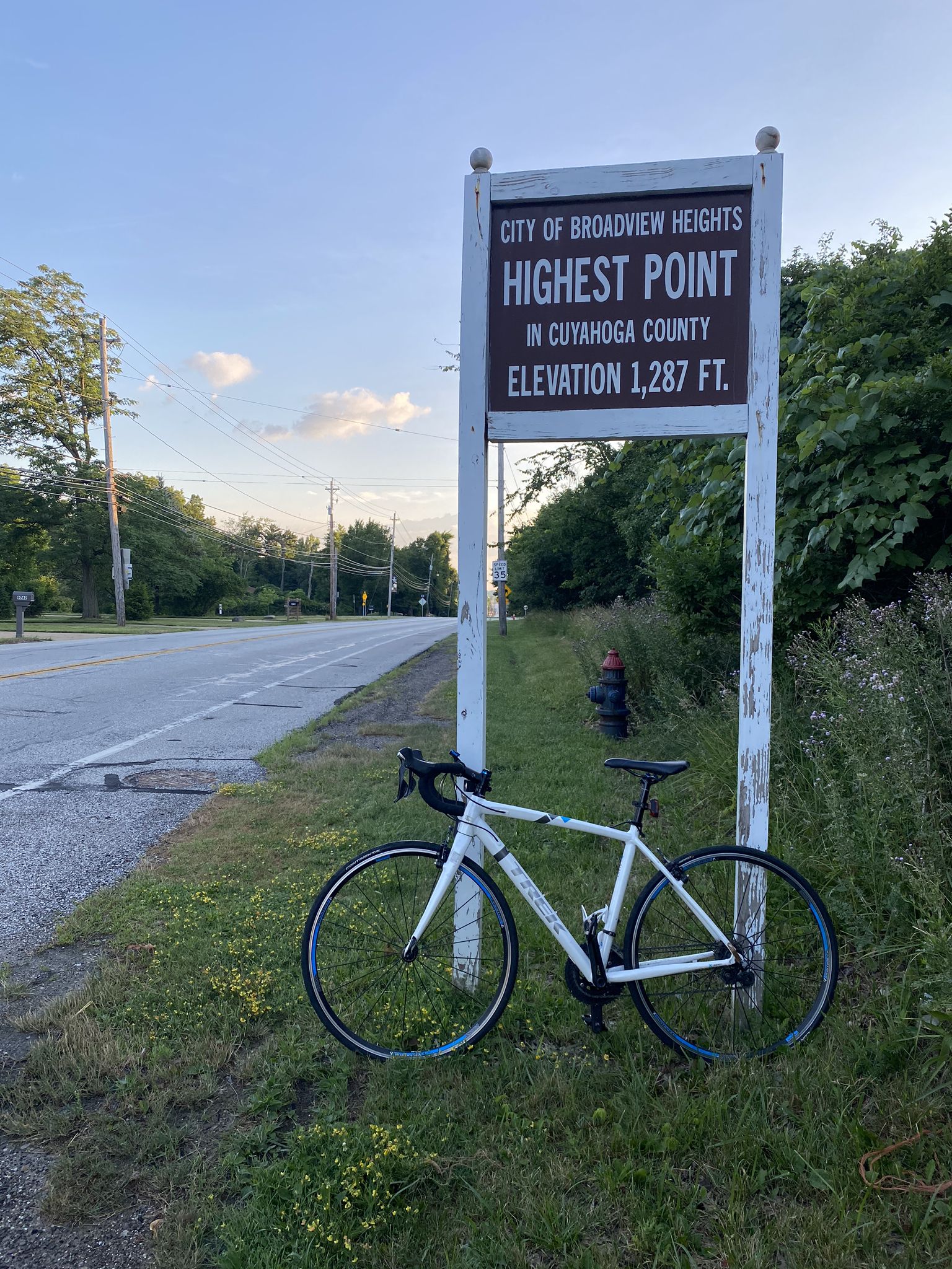 White road bike parked next to a wooden sign on a grassy roadside. - High Point loop