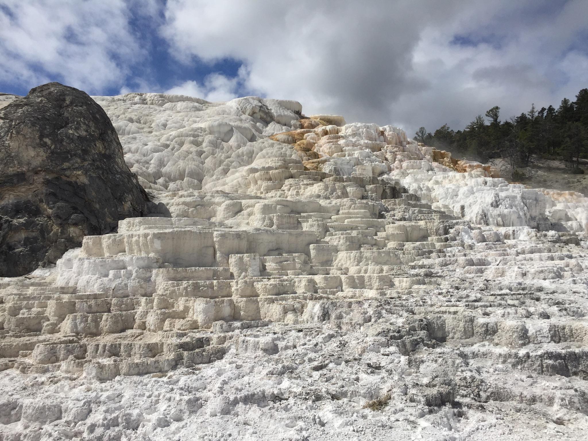 White and orange tiered mineral formations on a hillside under a cloudy sky.