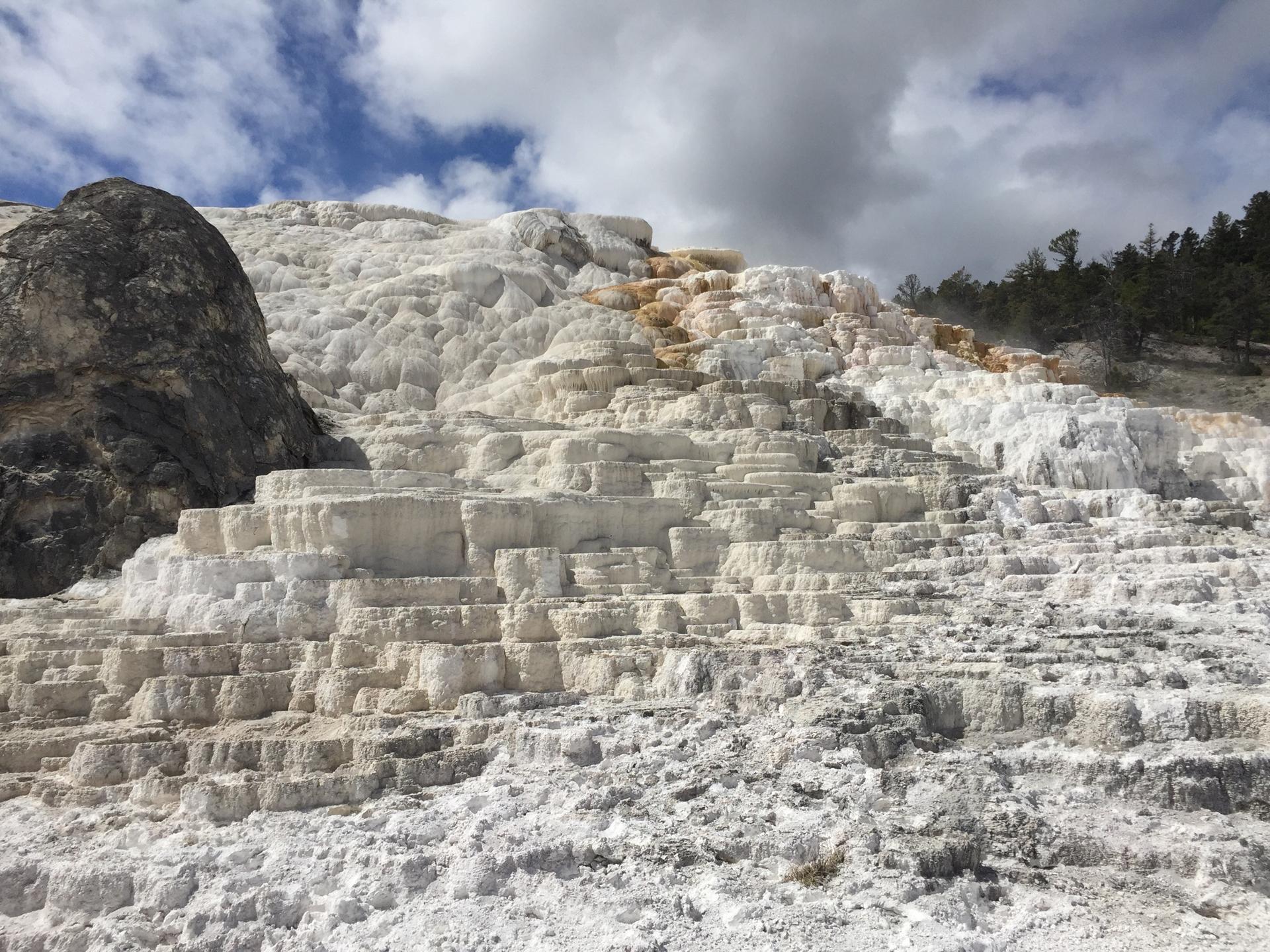White and orange tiered mineral formations on a hillside under a cloudy sky.