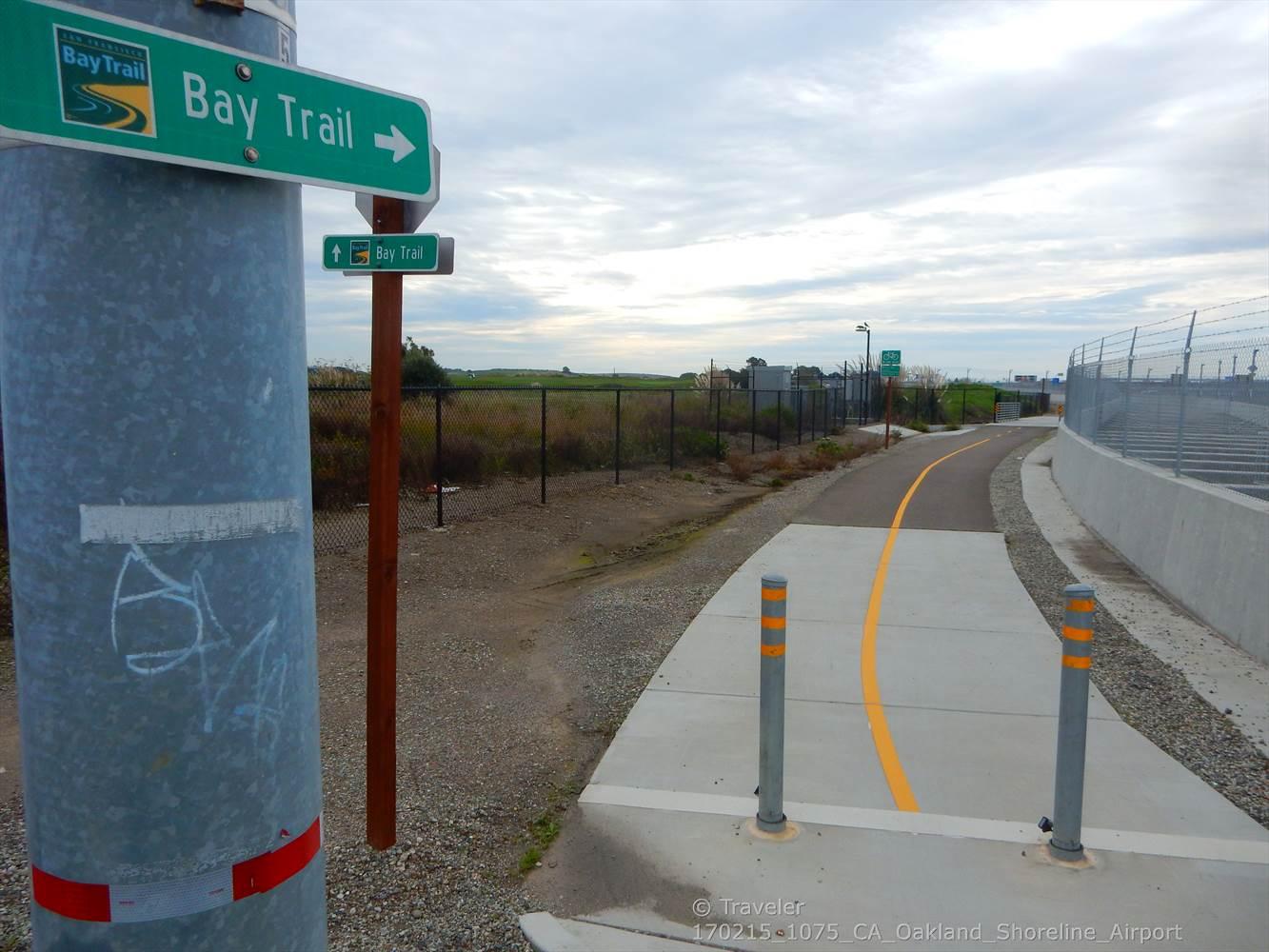 A paved path with a yellow line and a trail sign under a cloudy sky.