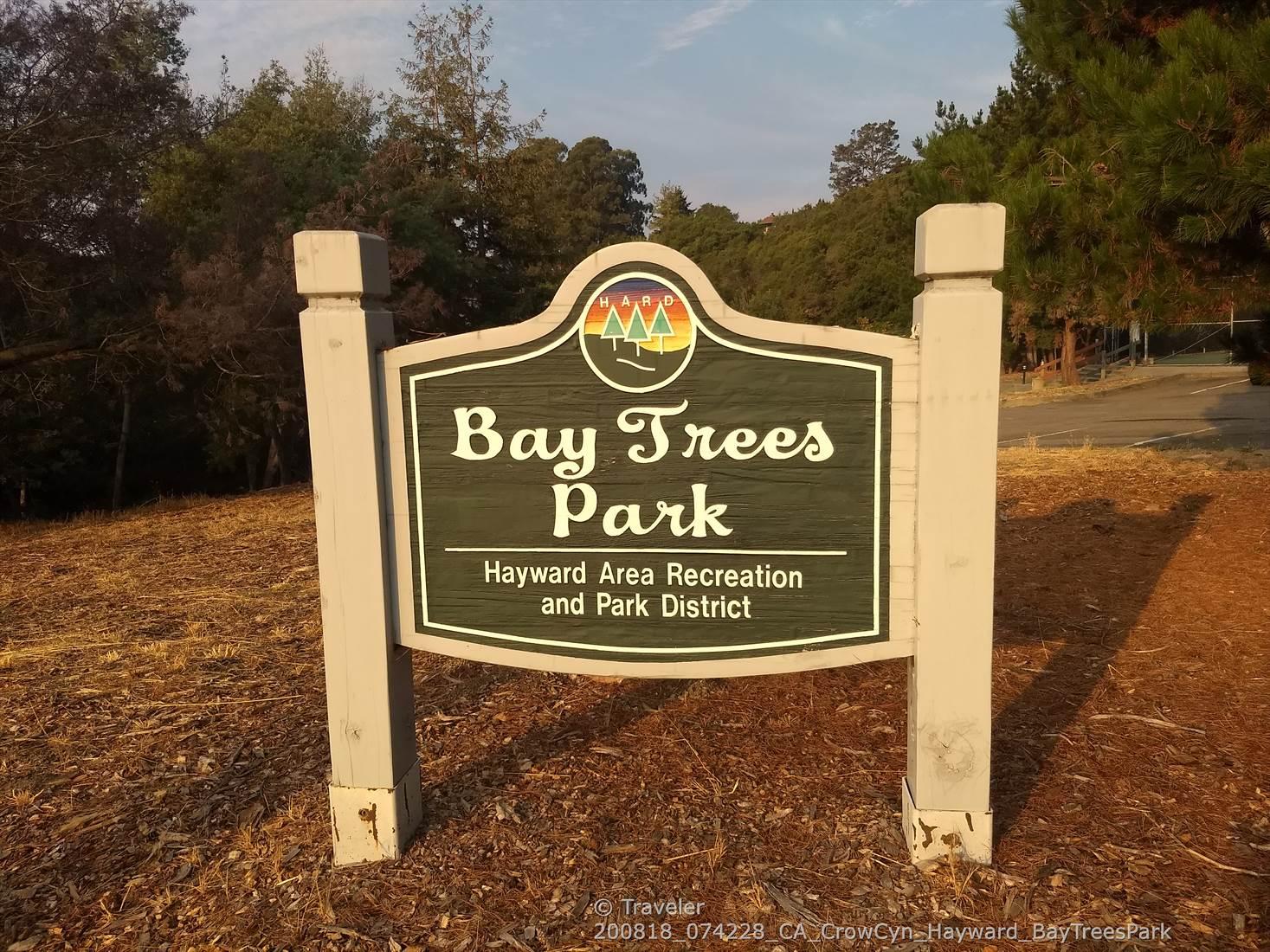 A wooden park sign with text, surrounded by trees under golden light.
