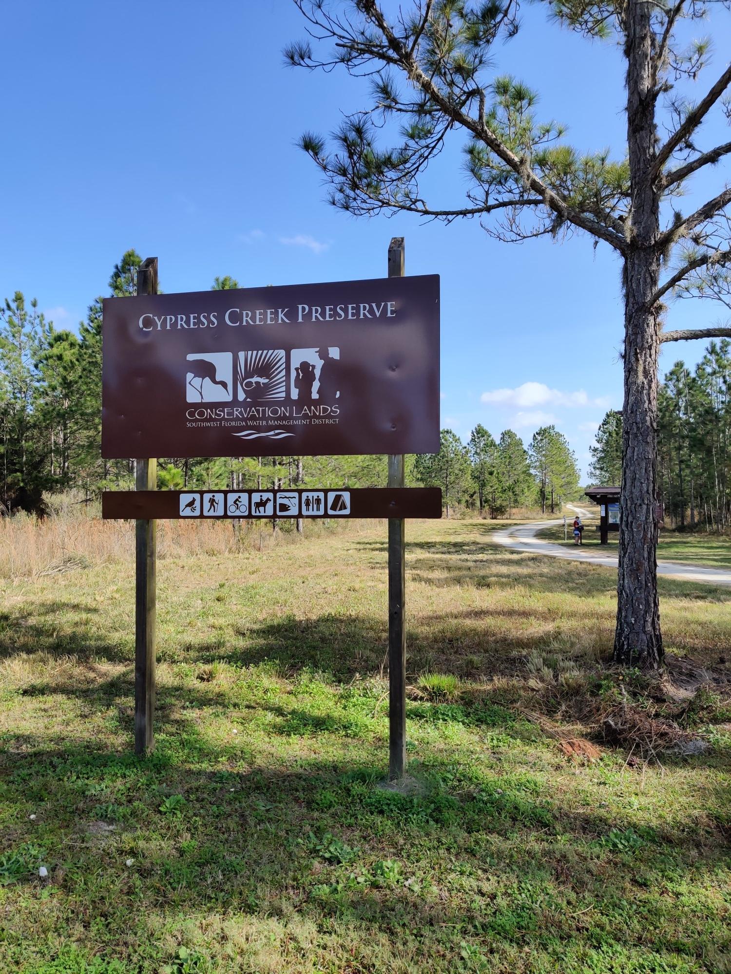 A large brown sign stands in a grassy field with pine trees.