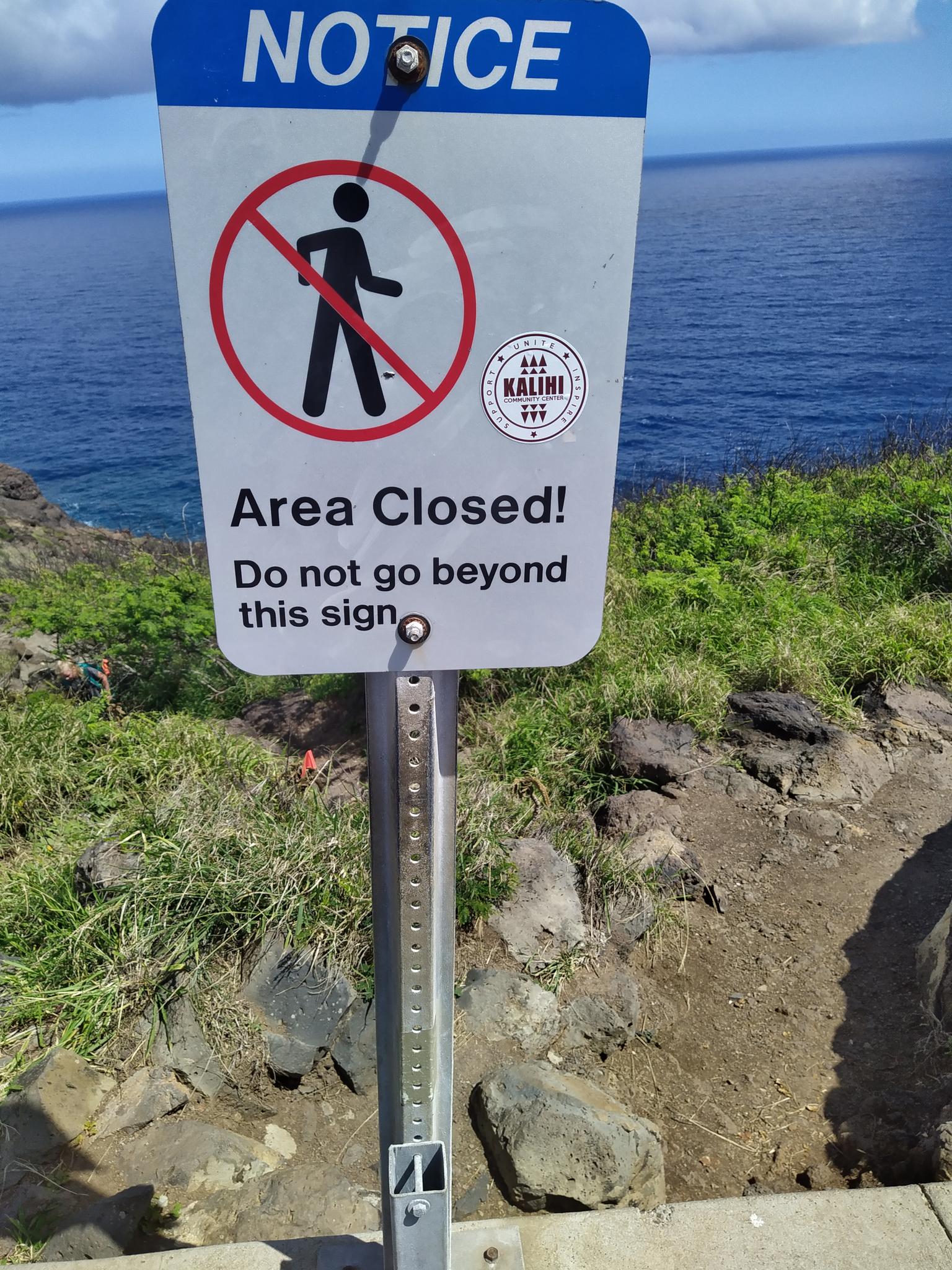 A "Notice Area Closed!" sign with a no-walking symbol, overlooking the ocean.