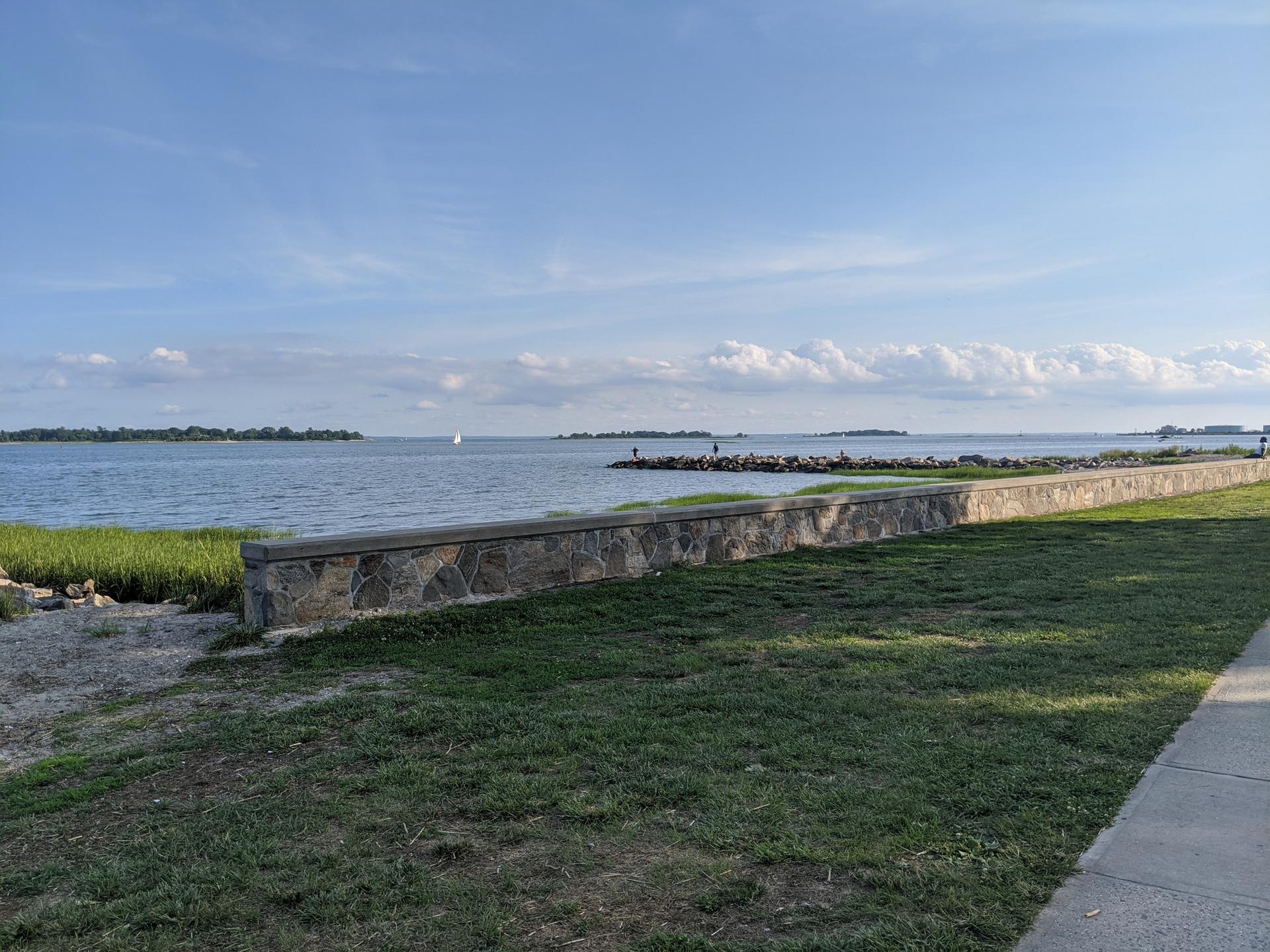 Sunny view of a wide bay with a stone wall and distant jetty.