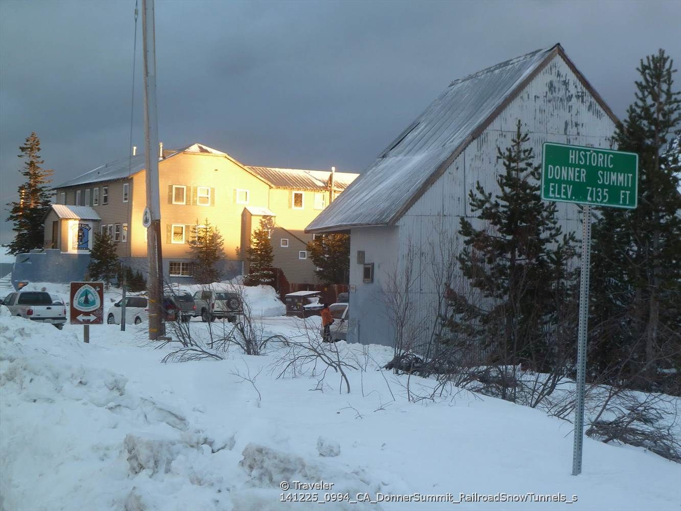 Snow-covered buildings and pine trees under a cloudy sky with sunlight. - Tahoe-Pyramid Bikeway and Donner Pass Loop
