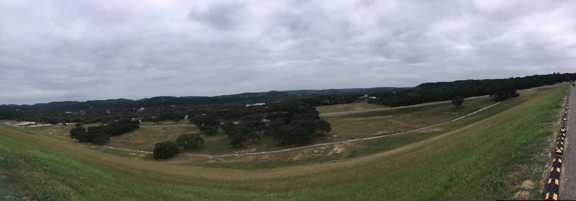 Panoramic view of a valley with grassy slopes and distant hills under an overcast sky.