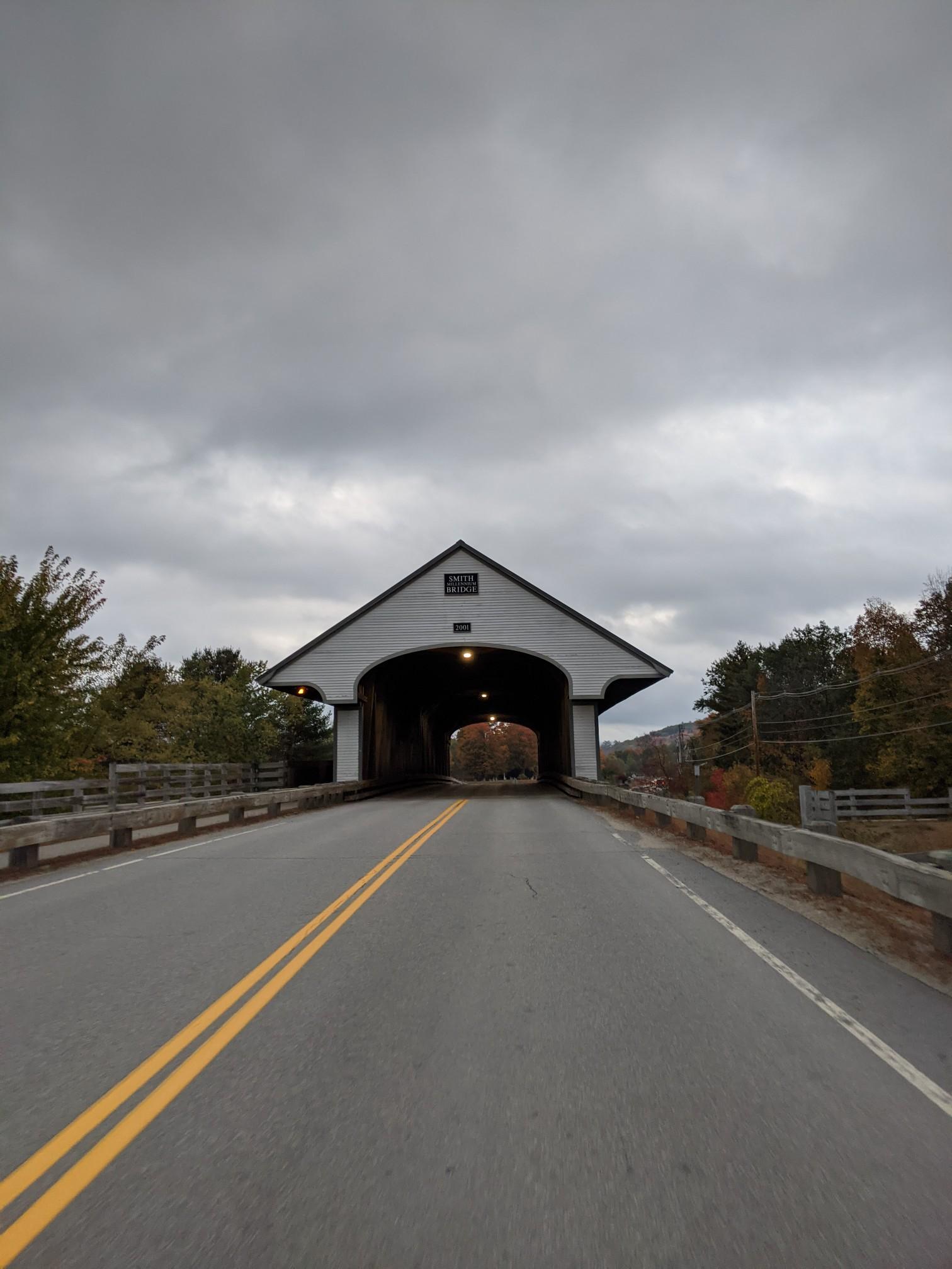 A long covered bridge over a road under a cloudy, overcast sky.
