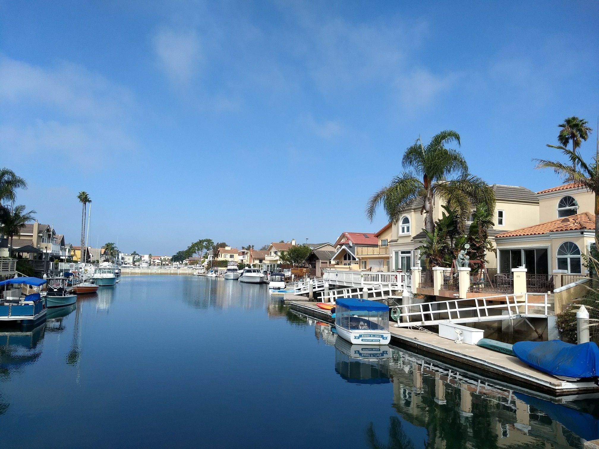 Sunny canal with houses, docked boats, and palm trees under a clear blue sky. - Channel Islands Harbor – Channel Island Harbor loop from Victoria & Hemlock (Southbound)