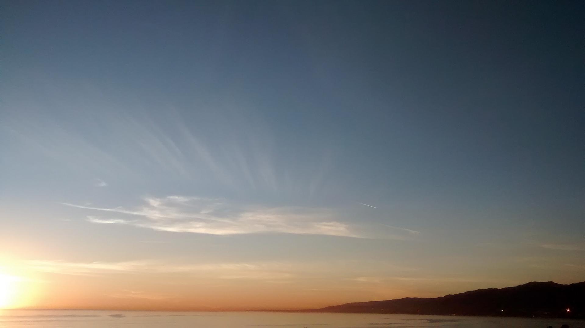 Sunset over calm ocean with distant mountains and wispy clouds.