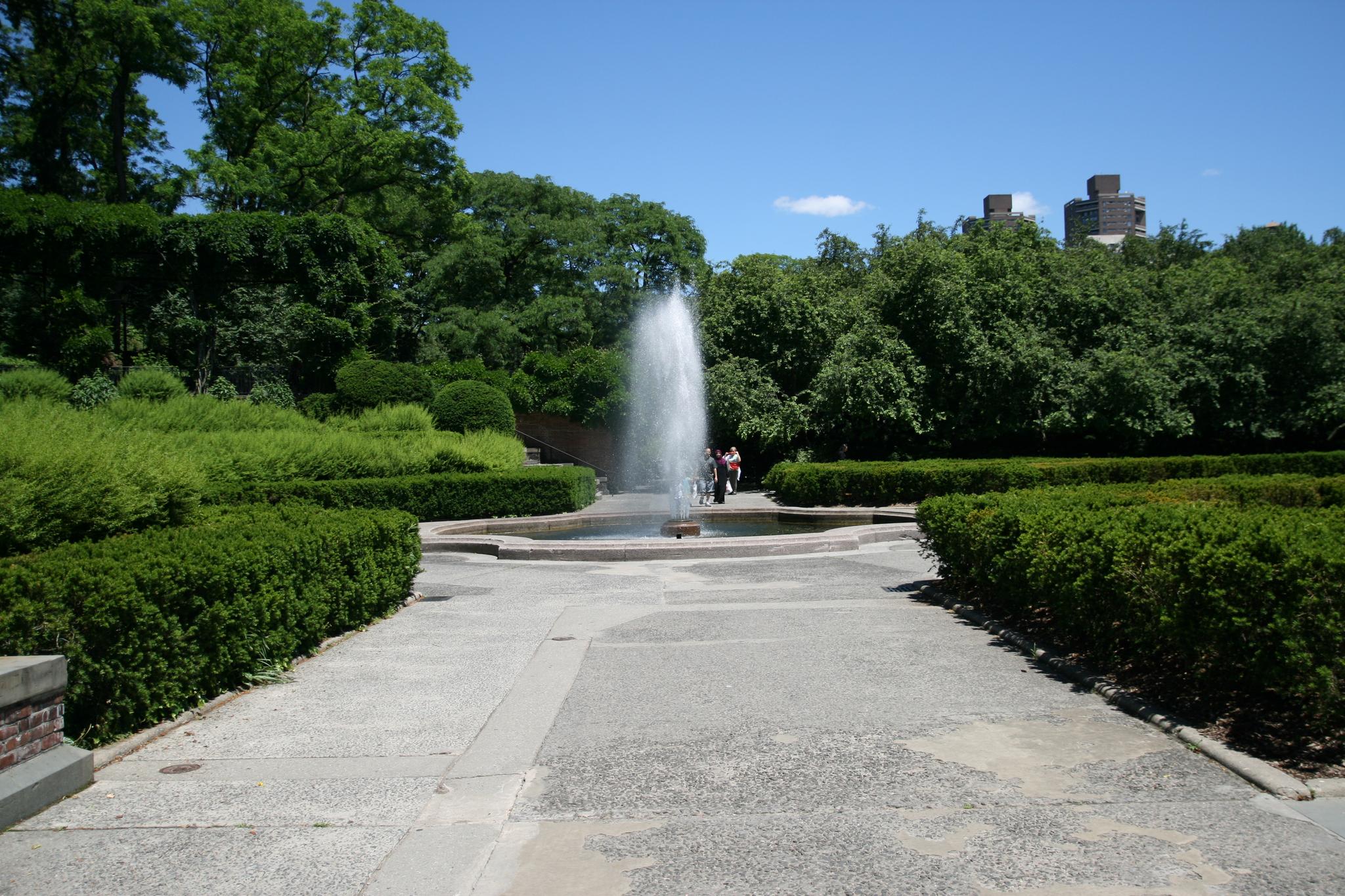 Large water fountain in a manicured garden with green hedges.
