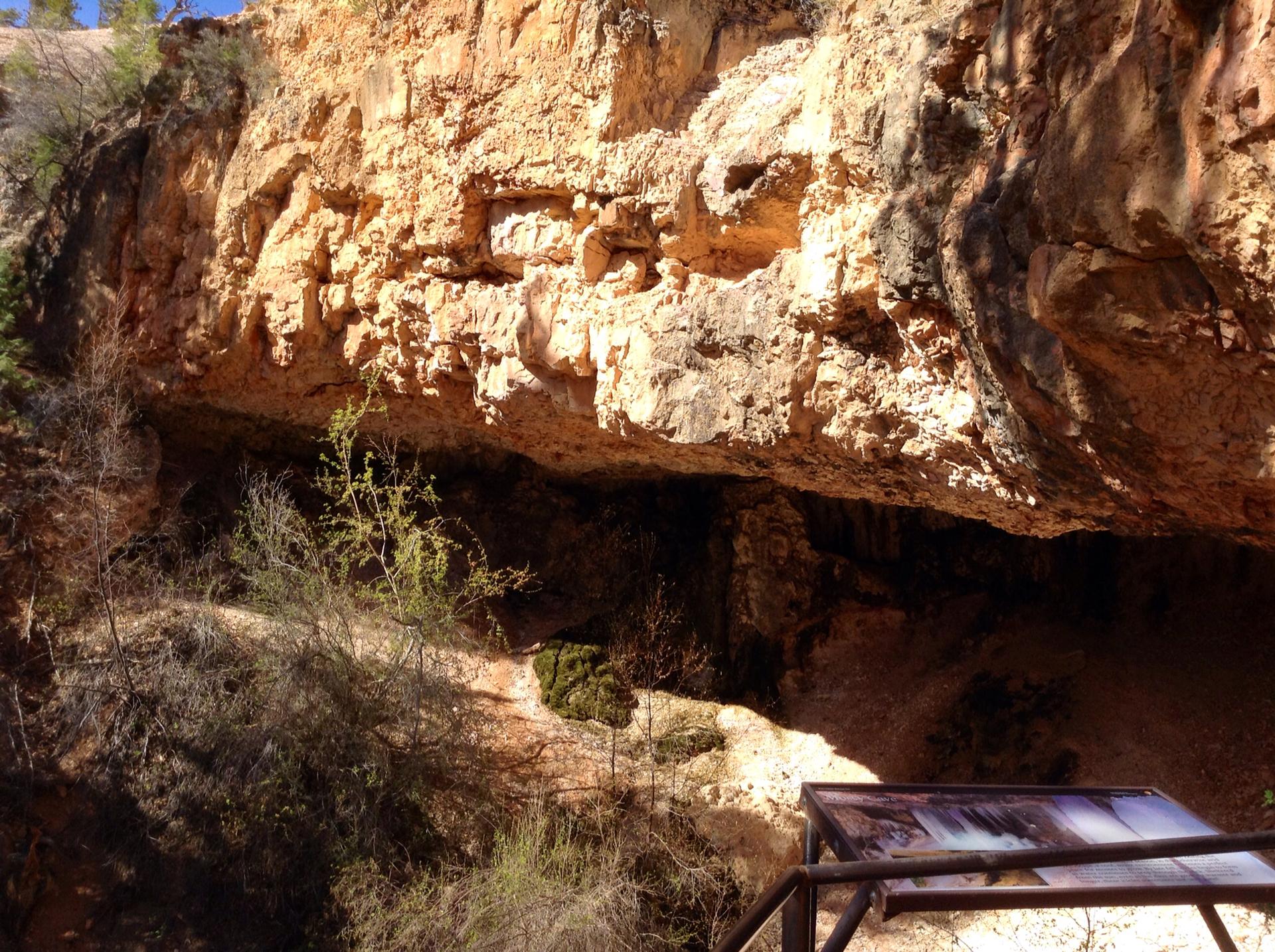 Large rock overhang with a dark cave opening and an informational sign.