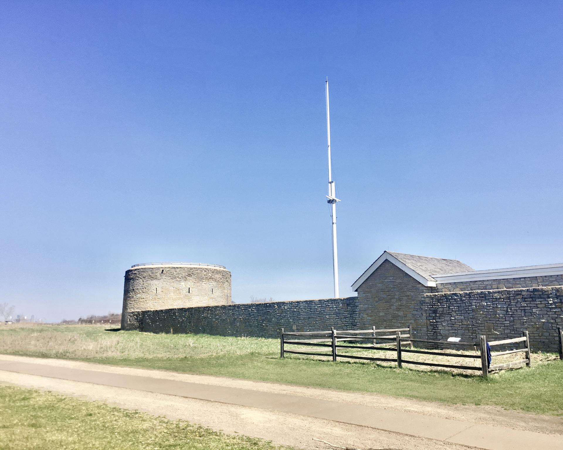 Stone fort and building with a tall flagpole under a clear blue sky.
