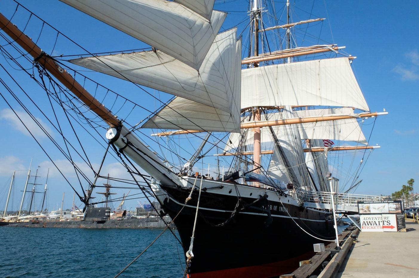 A large historic sailing ship with white sails docked at a pier.