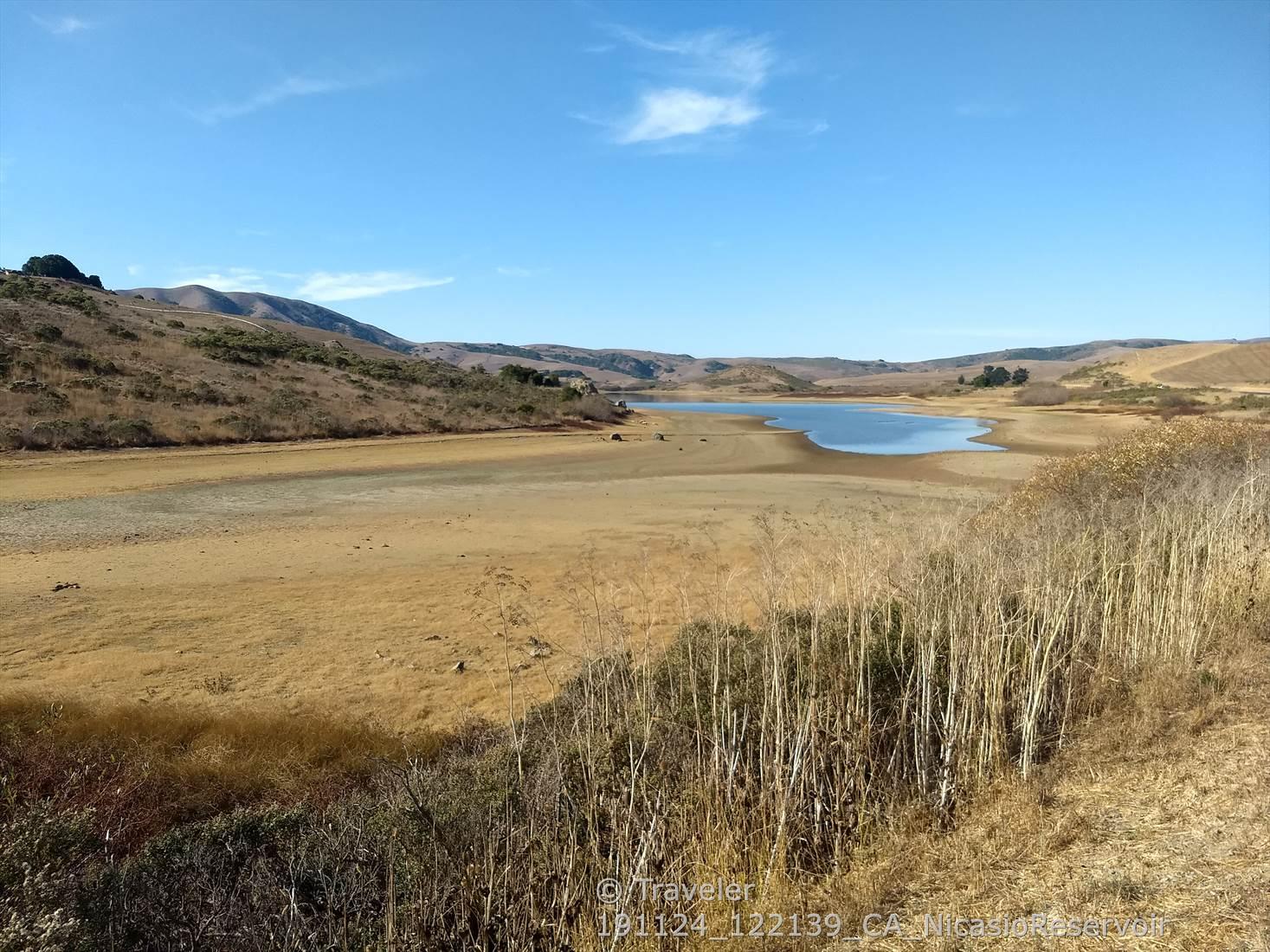 Expansive dry lakebed with a small body of water and distant hills.