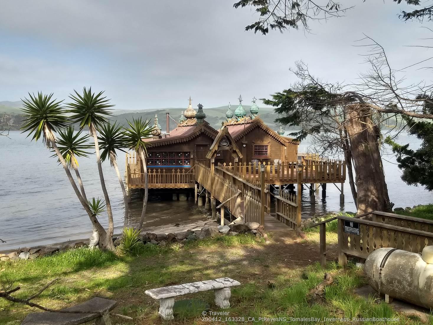 Ornate wooden building on stilts over water, with palm trees and a bench.