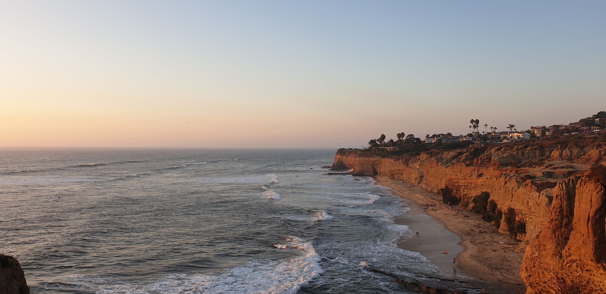 Warm sunset light illuminates coastal cliffs, a beach, and ocean waves. - Sunset Cliffs Loop Trail