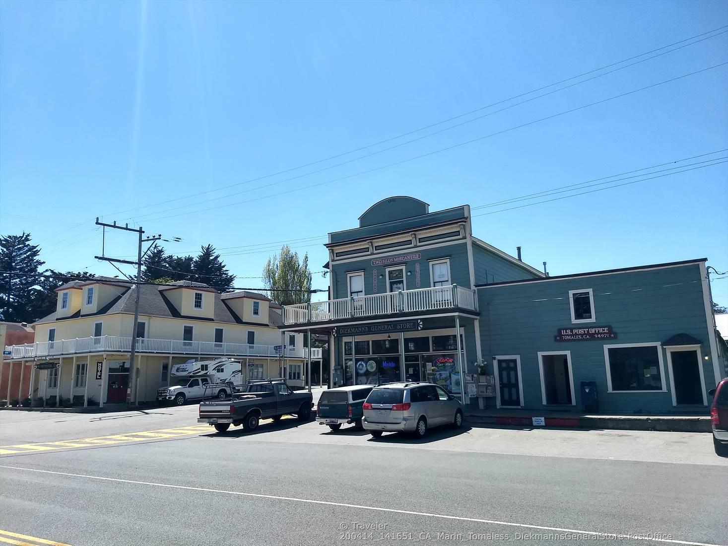 Two historic-looking buildings with cars parked on a sunny street.