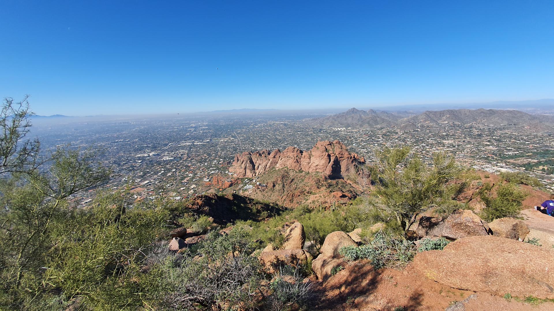 Expansive city view from rocky desert mountain under clear blue sky.