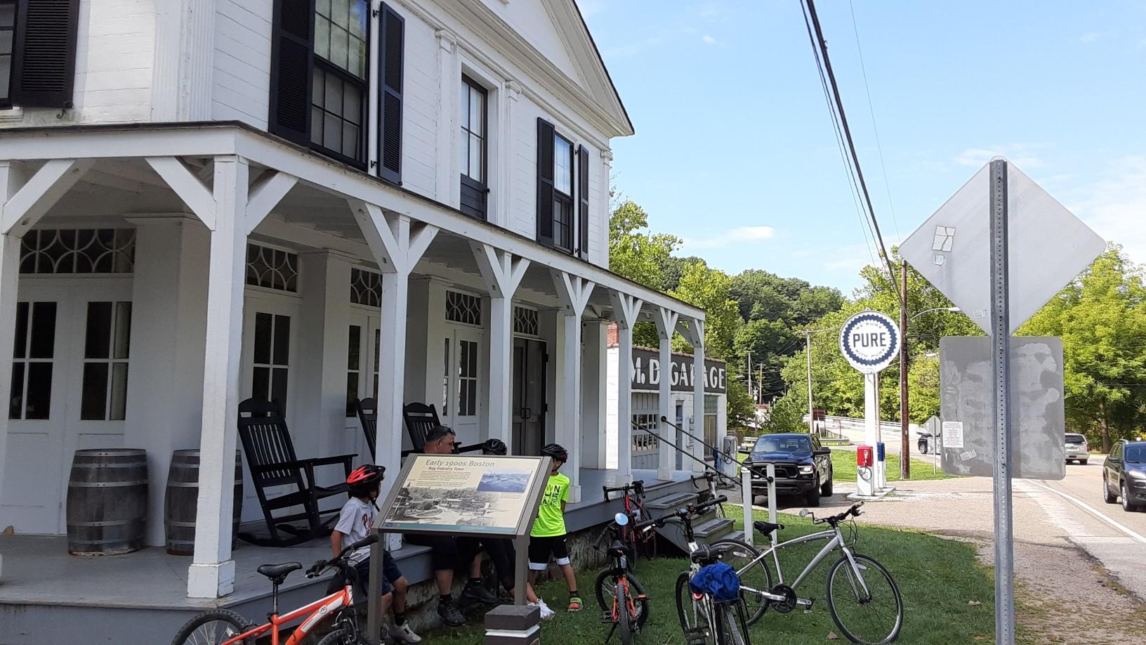 A white building with a porch, people, and bicycles on a sunny day.