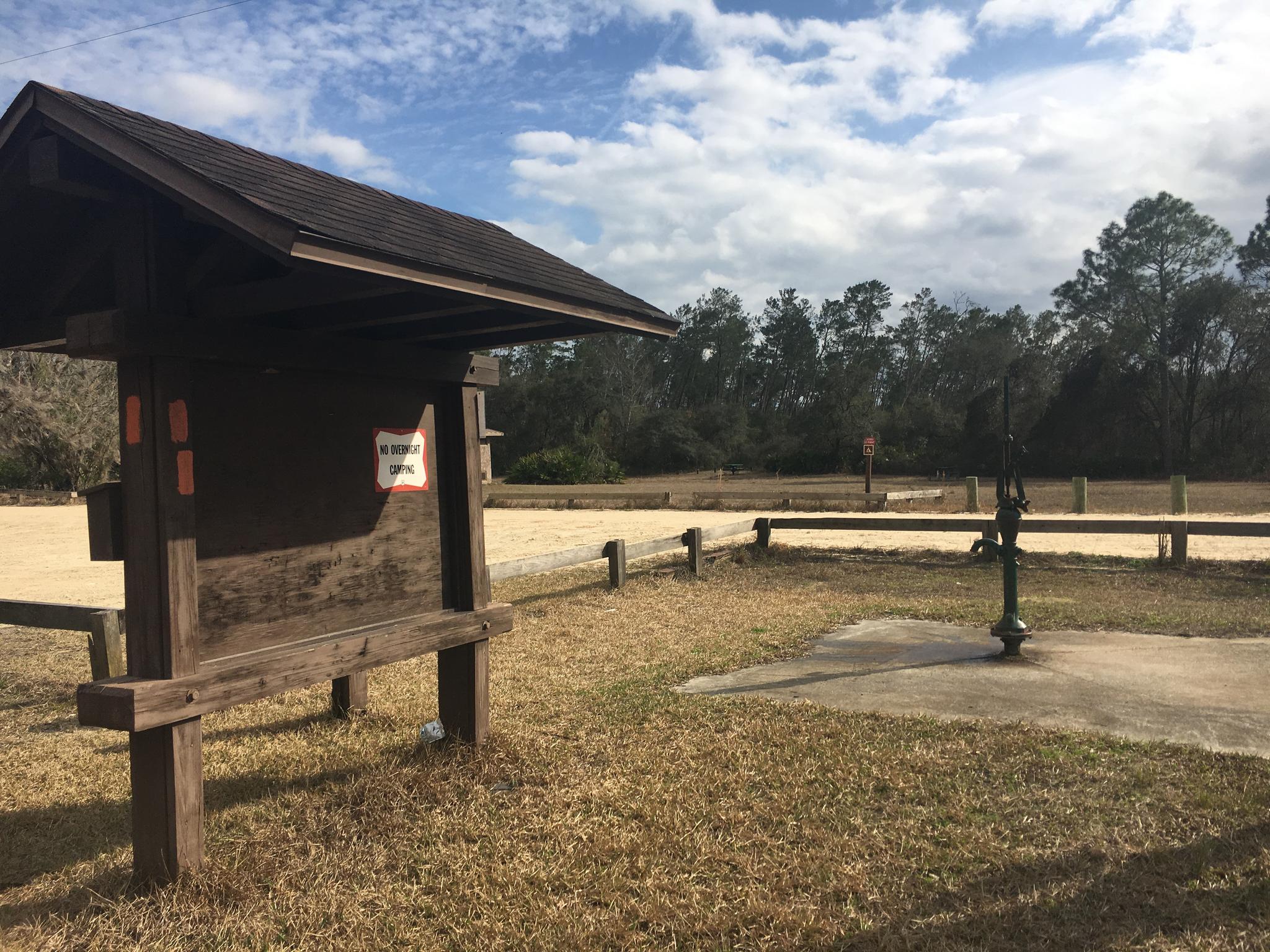 Wooden information kiosk and water pump in a dirt parking area.