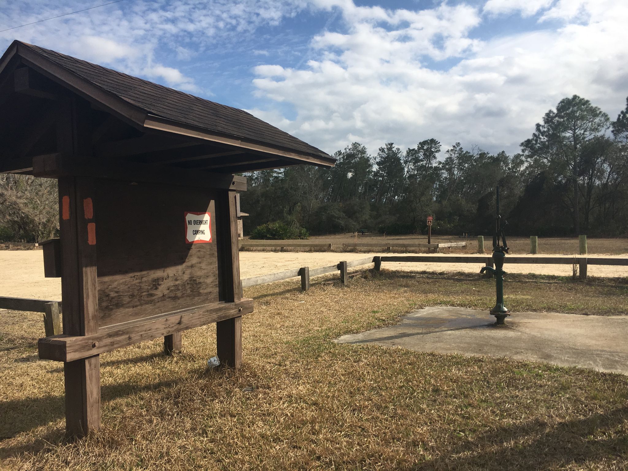 Wooden information kiosk and water pump in a dirt parking area. - Florida Trail: Alexander Springs to Juniper Springs