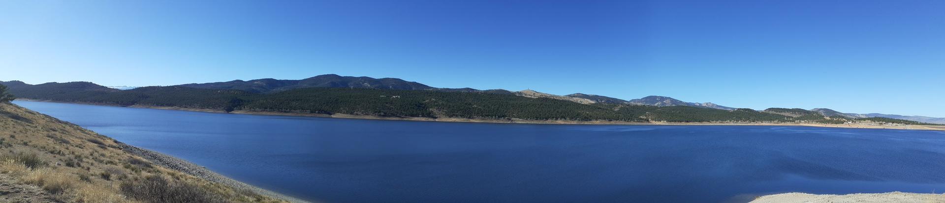 Panoramic view of a wide blue lake surrounded by mountains under clear sky.