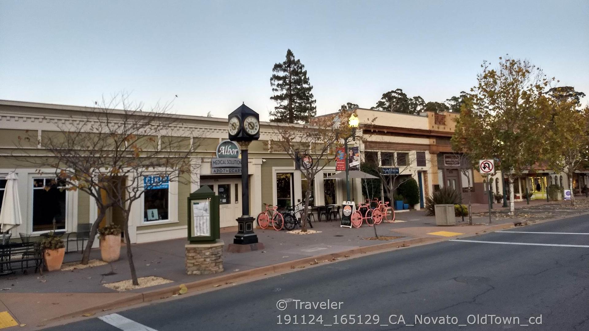 A street scene with storefronts, outdoor seating, and a prominent clock tower.