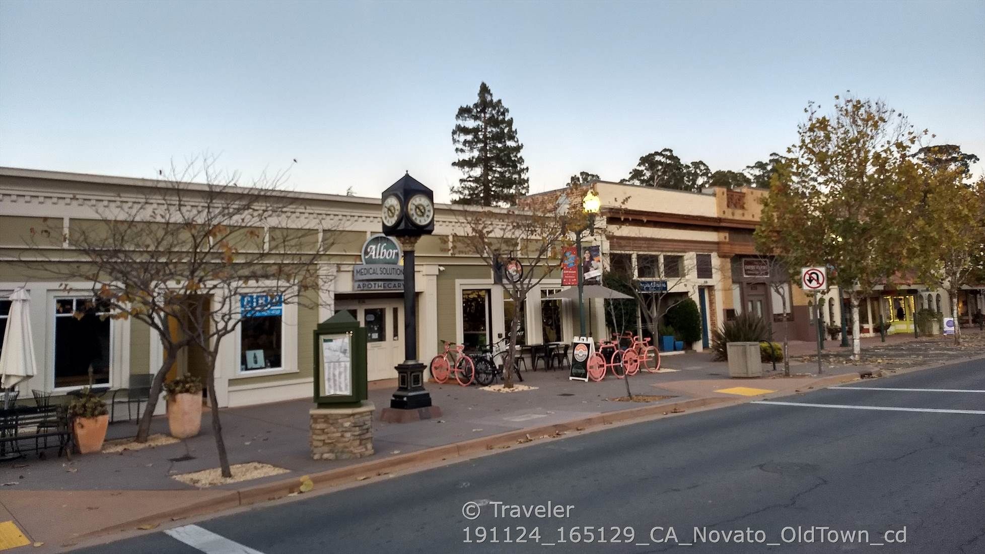 A street scene with storefronts, outdoor seating, and a prominent clock tower. - Novato City Hall – Old Town Novato loop from Novato Downtown