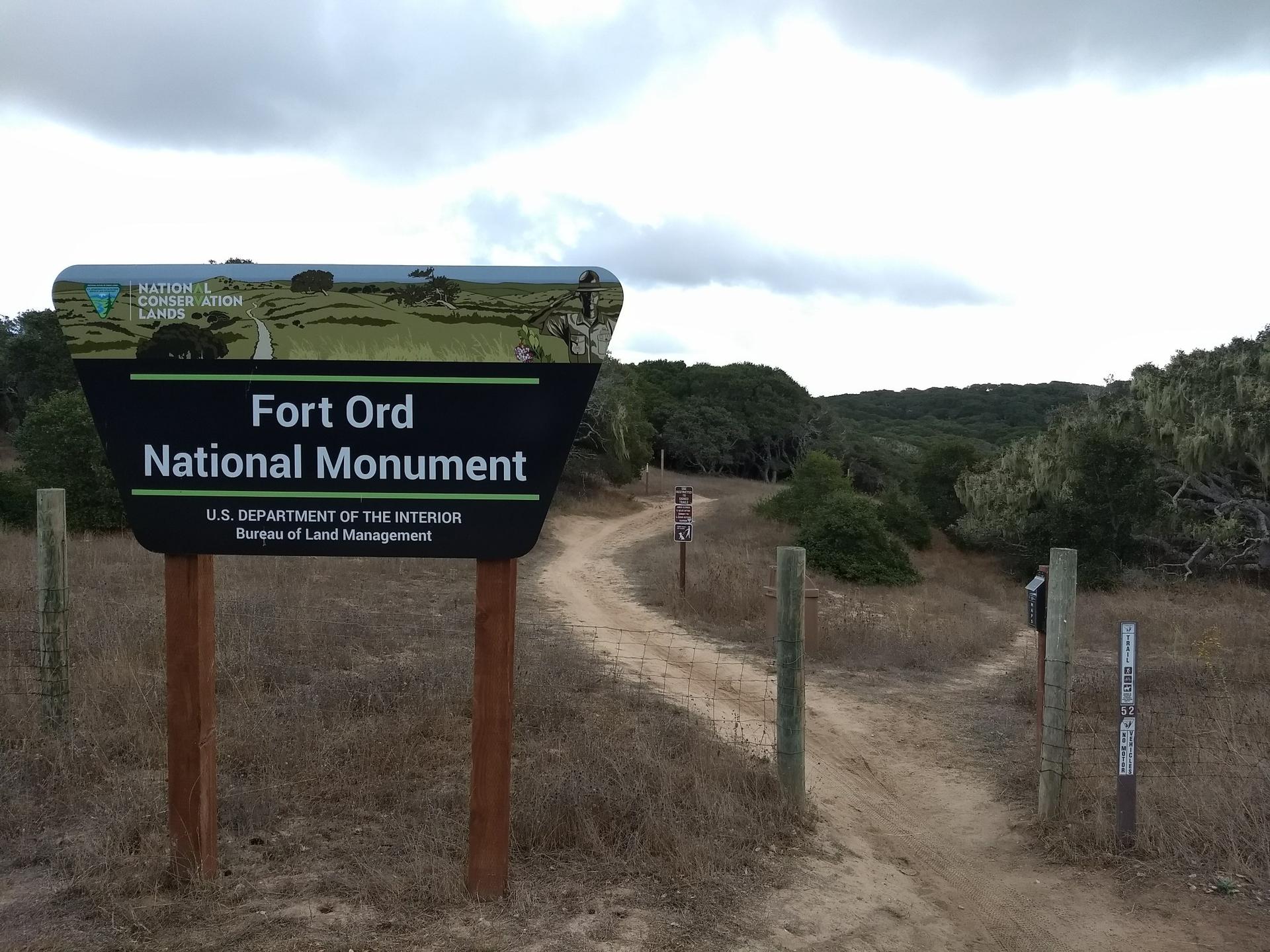 Large sign next to a dirt path leading into a wooded area.