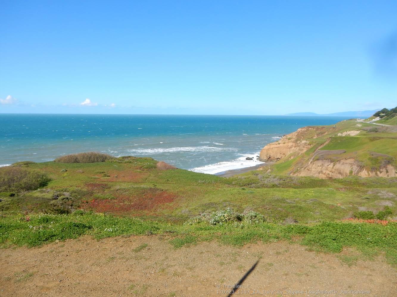 Expansive view of green coastal hillsides meeting a rocky ocean shoreline.