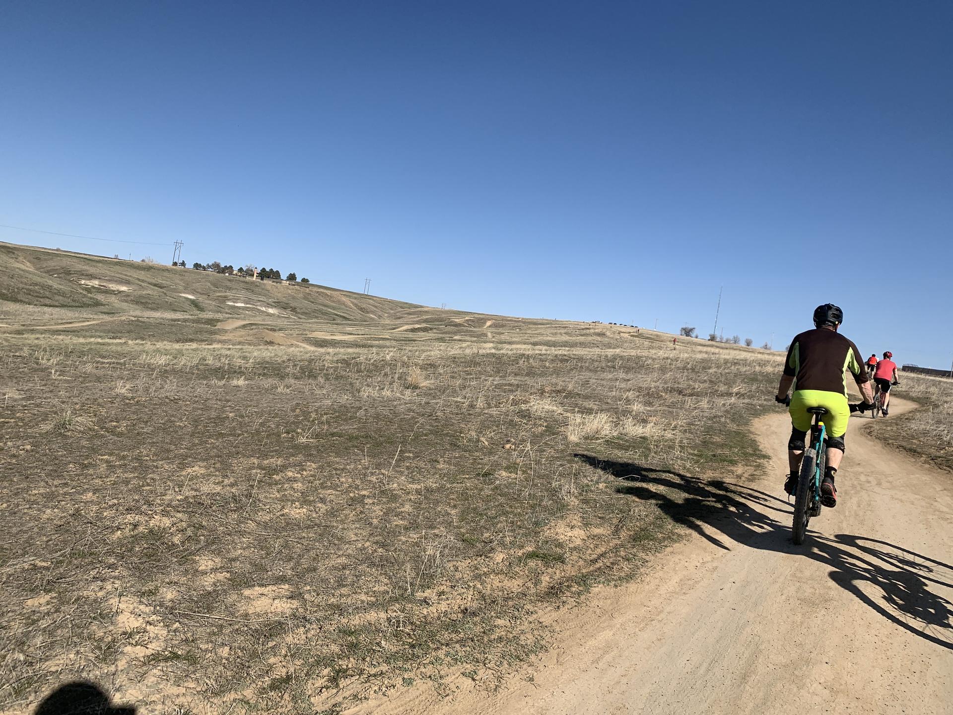 A person mountain biking on a dirt path in a sunny, dry, hilly landscape.