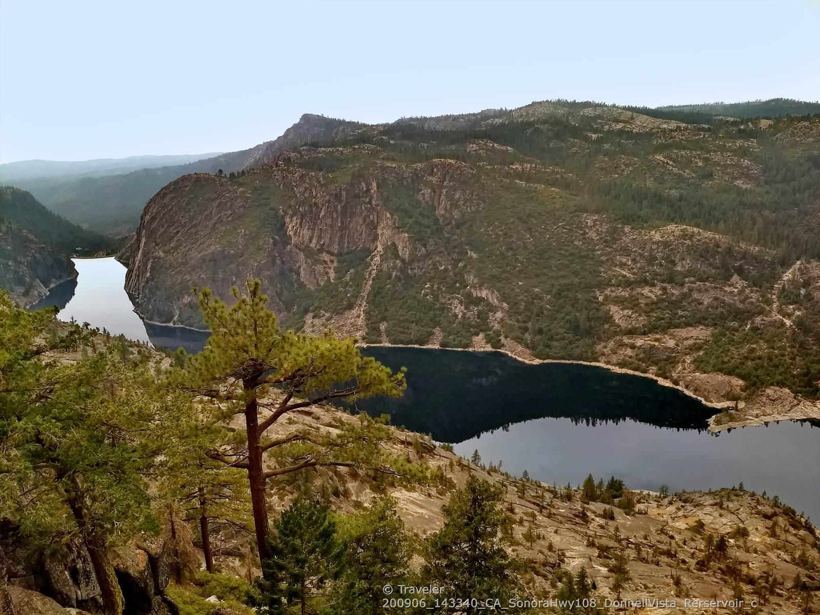 Dark lake surrounded by steep, forested mountains under a cloudy sky.