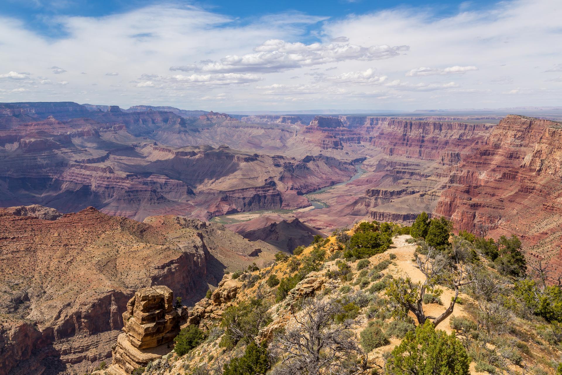 Expansive canyon vista with layered rock formations under a bright, cloudy sky.