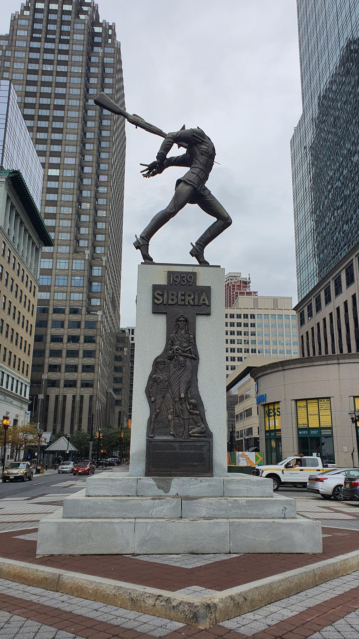 Bronze statue of a man swinging a bat in an urban setting.
