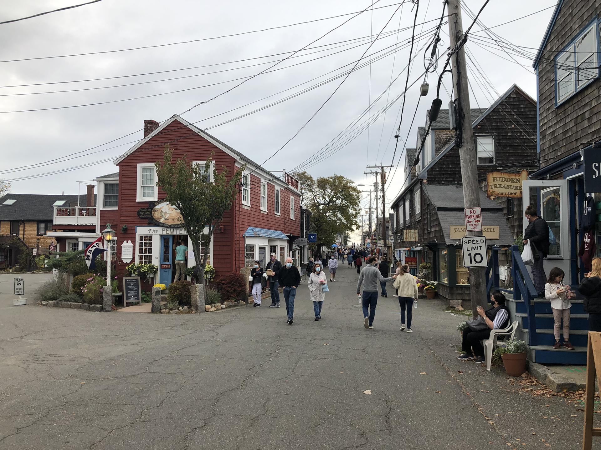 People walk on a street lined with colorful buildings and overhead wires.