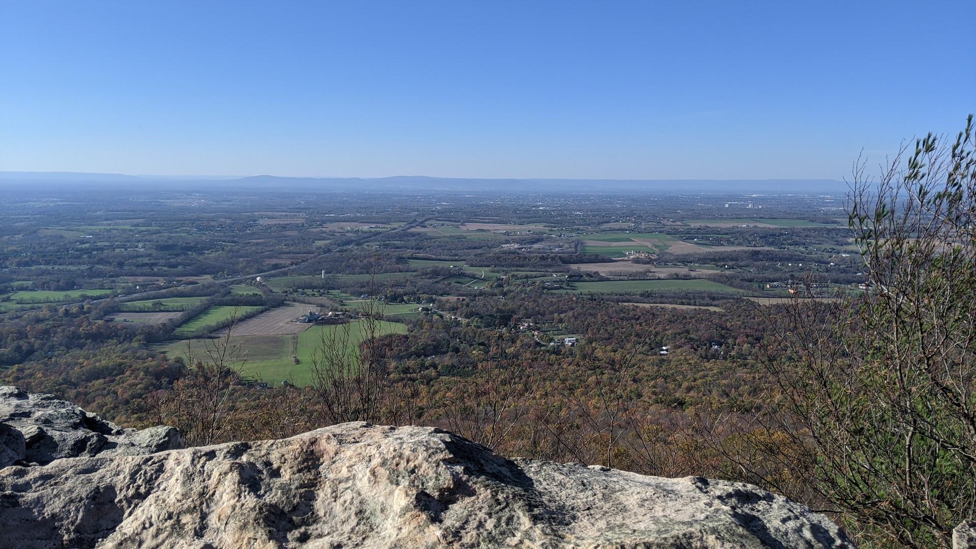 Sunny panoramic view of a wide valley with forests and fields.