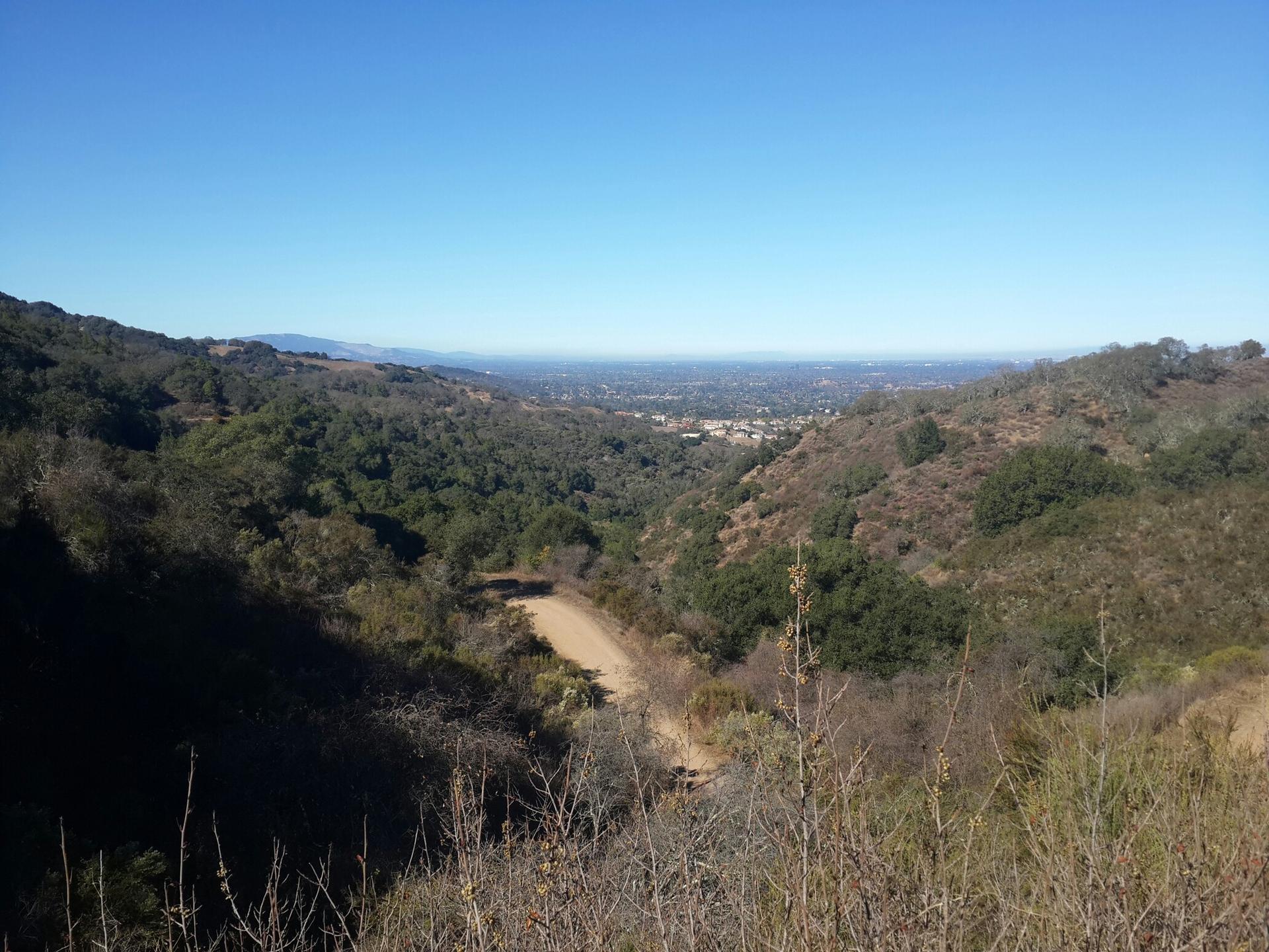 Wide view of a green valley with a distant town under clear skies.