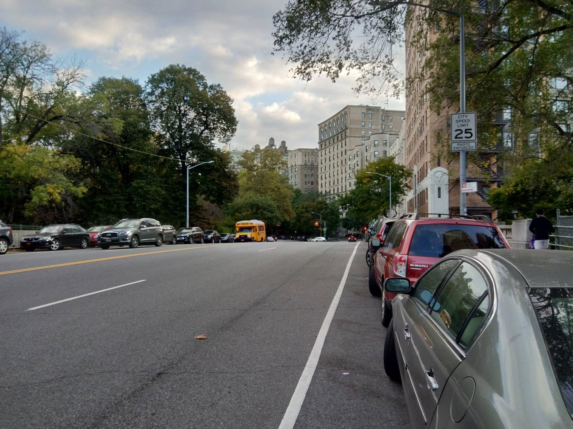 A street lined with parked cars and buildings under a cloudy sky.