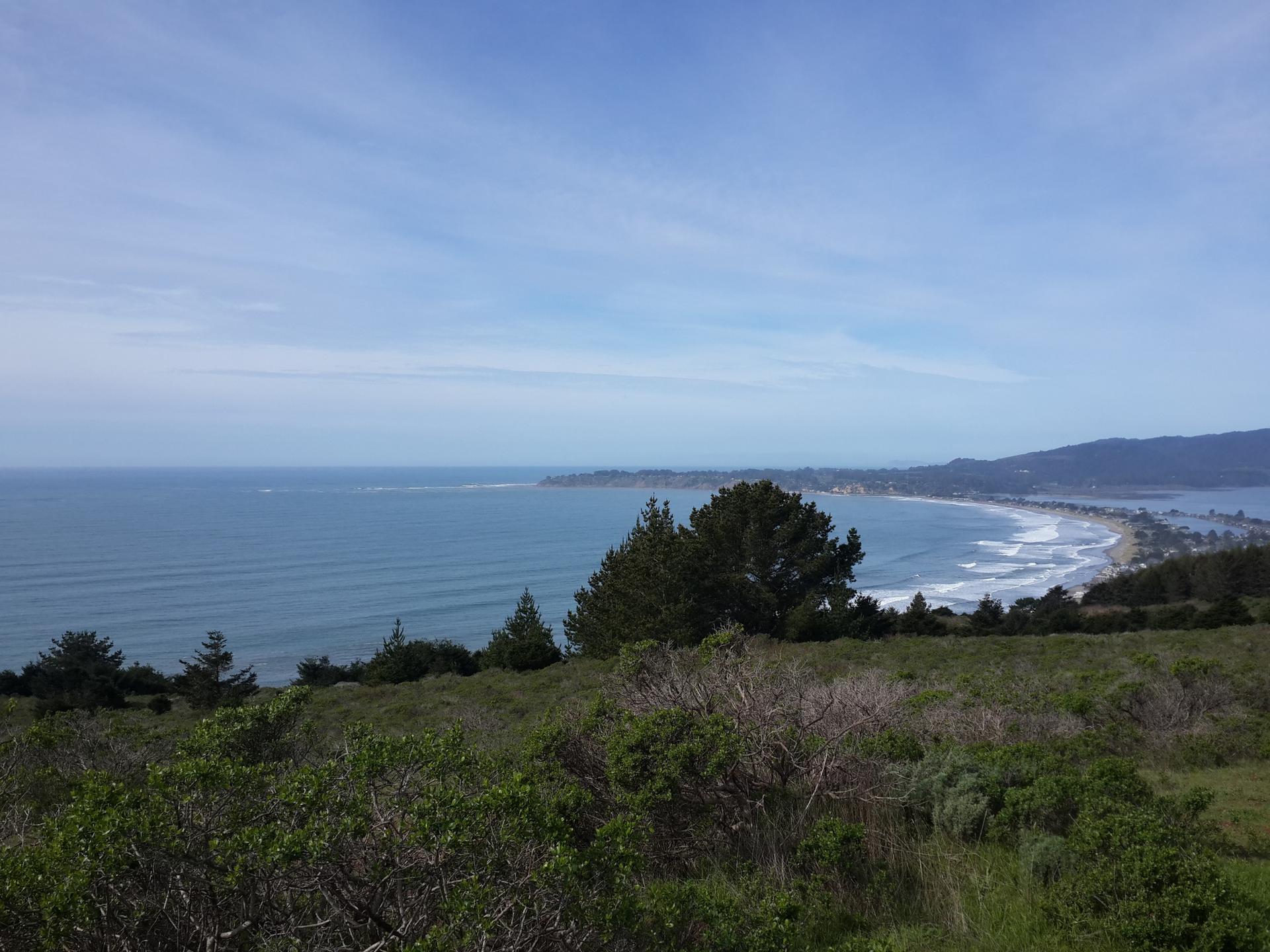 Overcast coastal landscape with ocean, distant beach, and green hills.