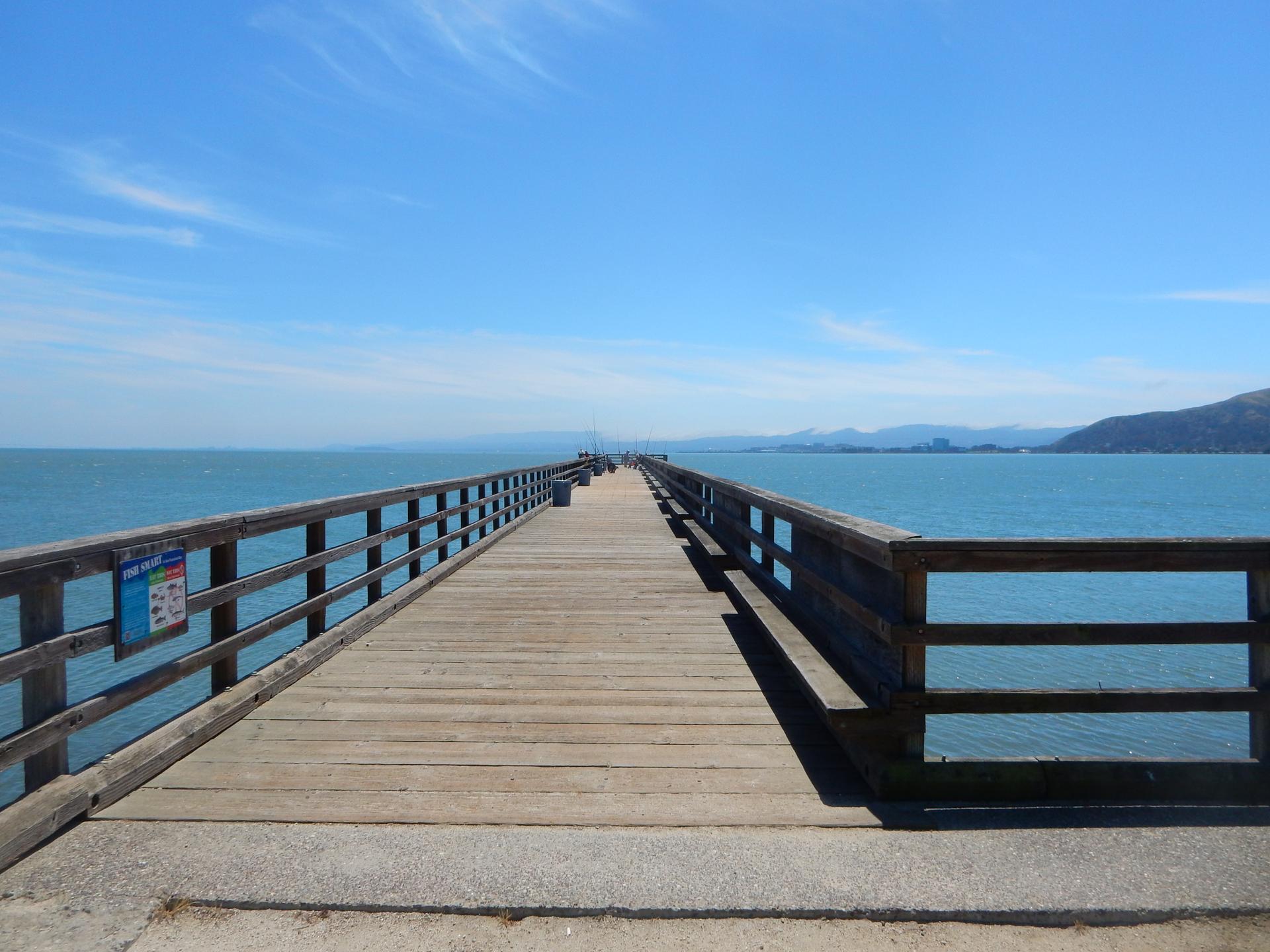 Long wooden pier extending into the ocean under a bright blue sky.