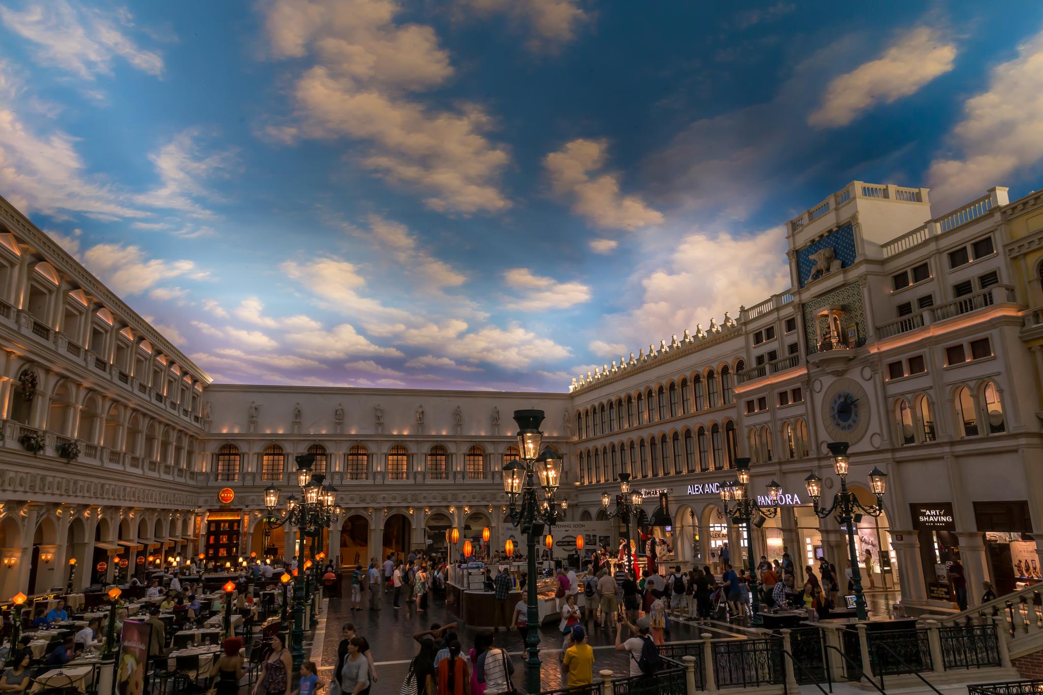 Bustling indoor plaza with ornate buildings and a painted sky ceiling.